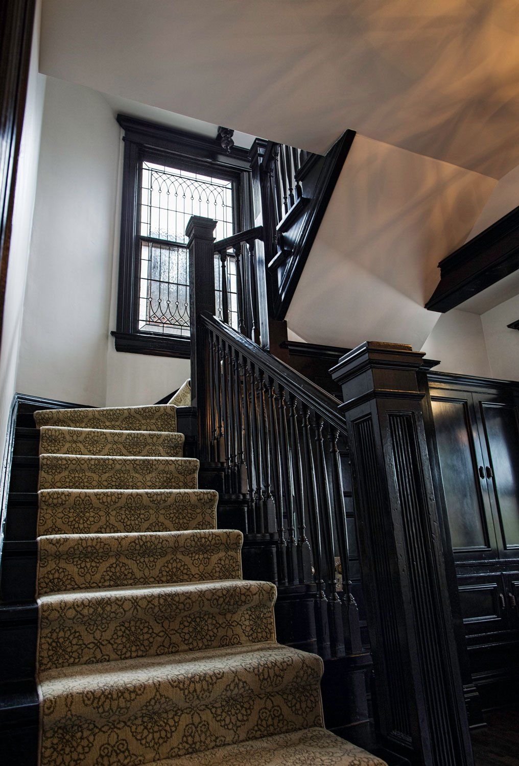 The main stairway is painted in lush black with a cushioned runner. We added closet doors at the mudroom below the stairs. There's a leaded glass window at the first landing, letting light into the stairwell.