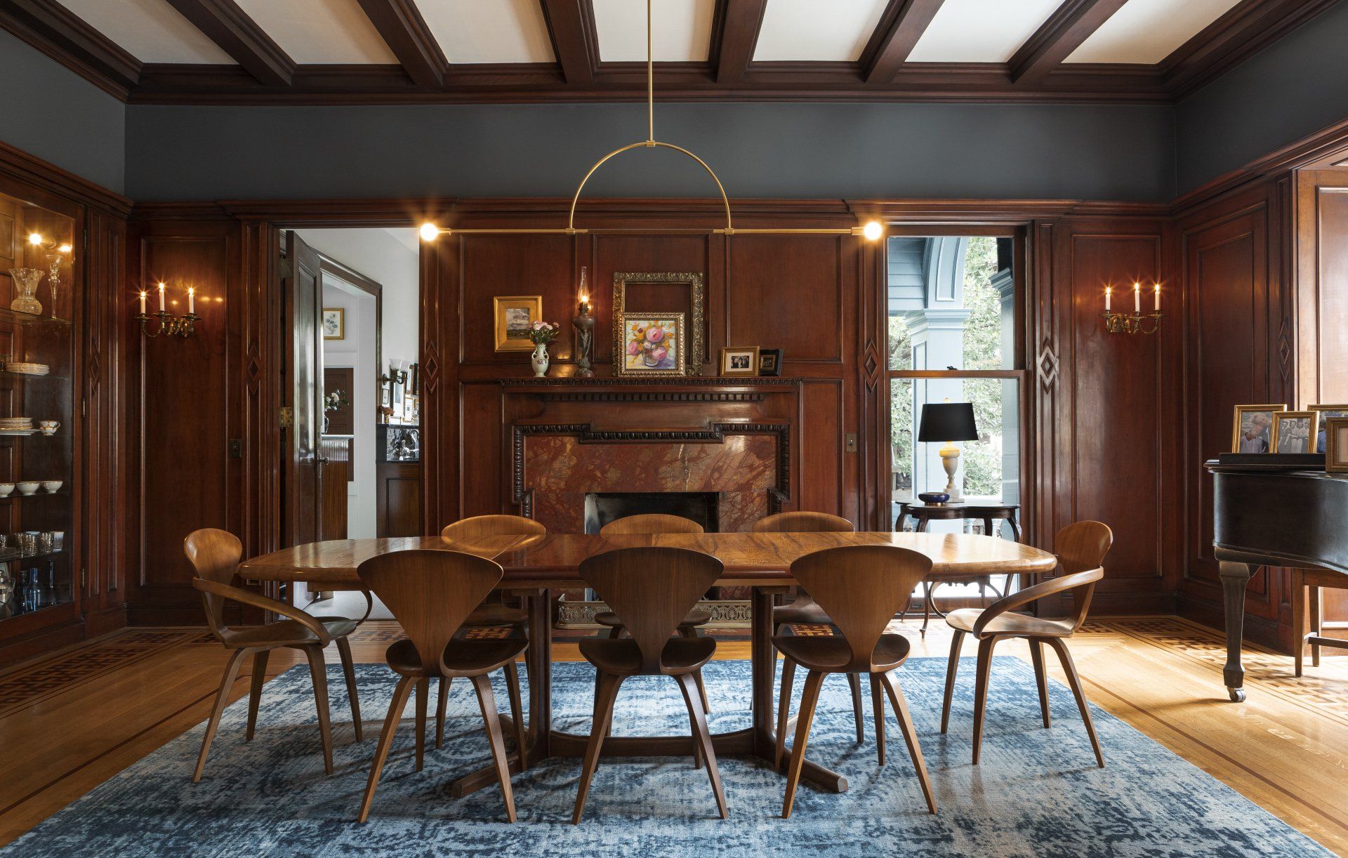 A moody dining room clad in elaborate mahogany millwork with a large fireplace and midcentury modern dining room set.