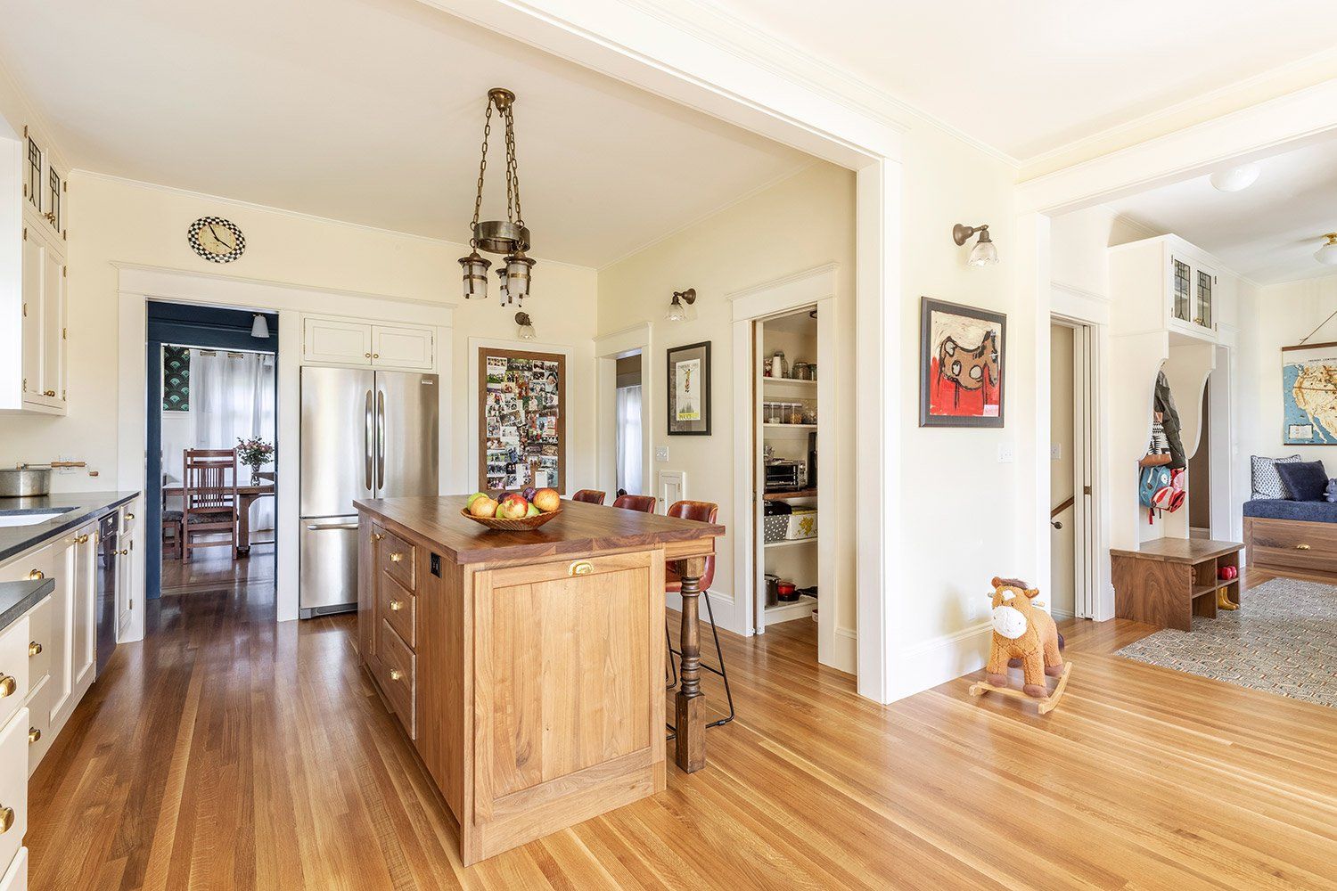 View of the kitchen and hallway from the back of the house, with the stain grade island, hardwood floors and white perimeter cabinets that match the walls and ceiling