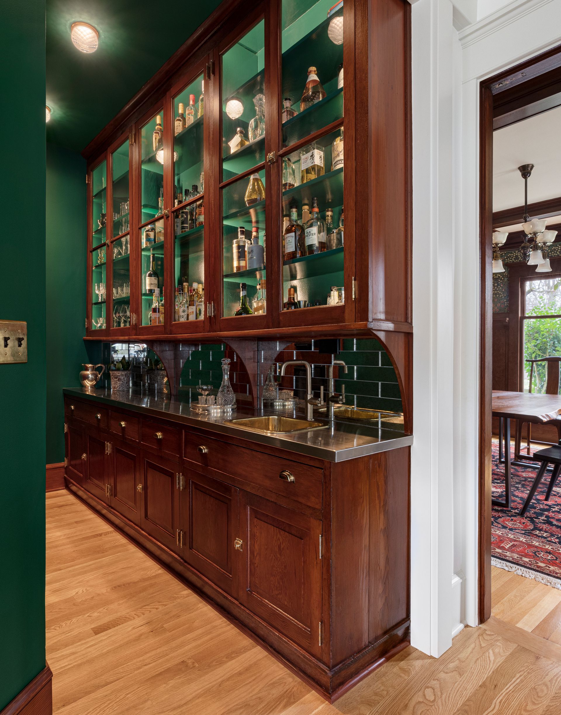 Former butler’s pantry fir cabinets now serve as a bar with new stainless steel counters, antique mirror glass tile backsplash and emerald-green walls. 
