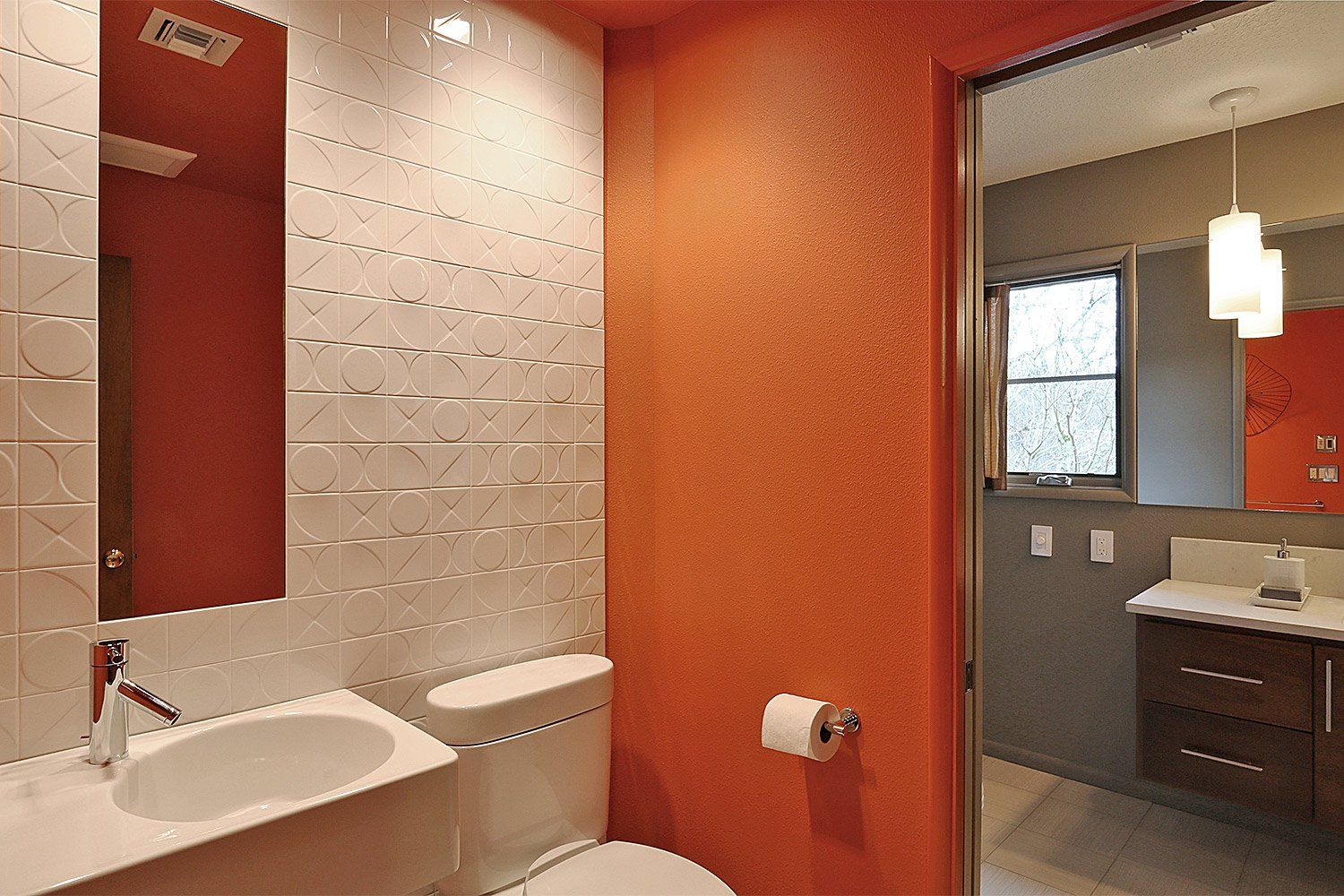 In the WC, clementine colored walls & white 4x4 geometric relief tiles add character