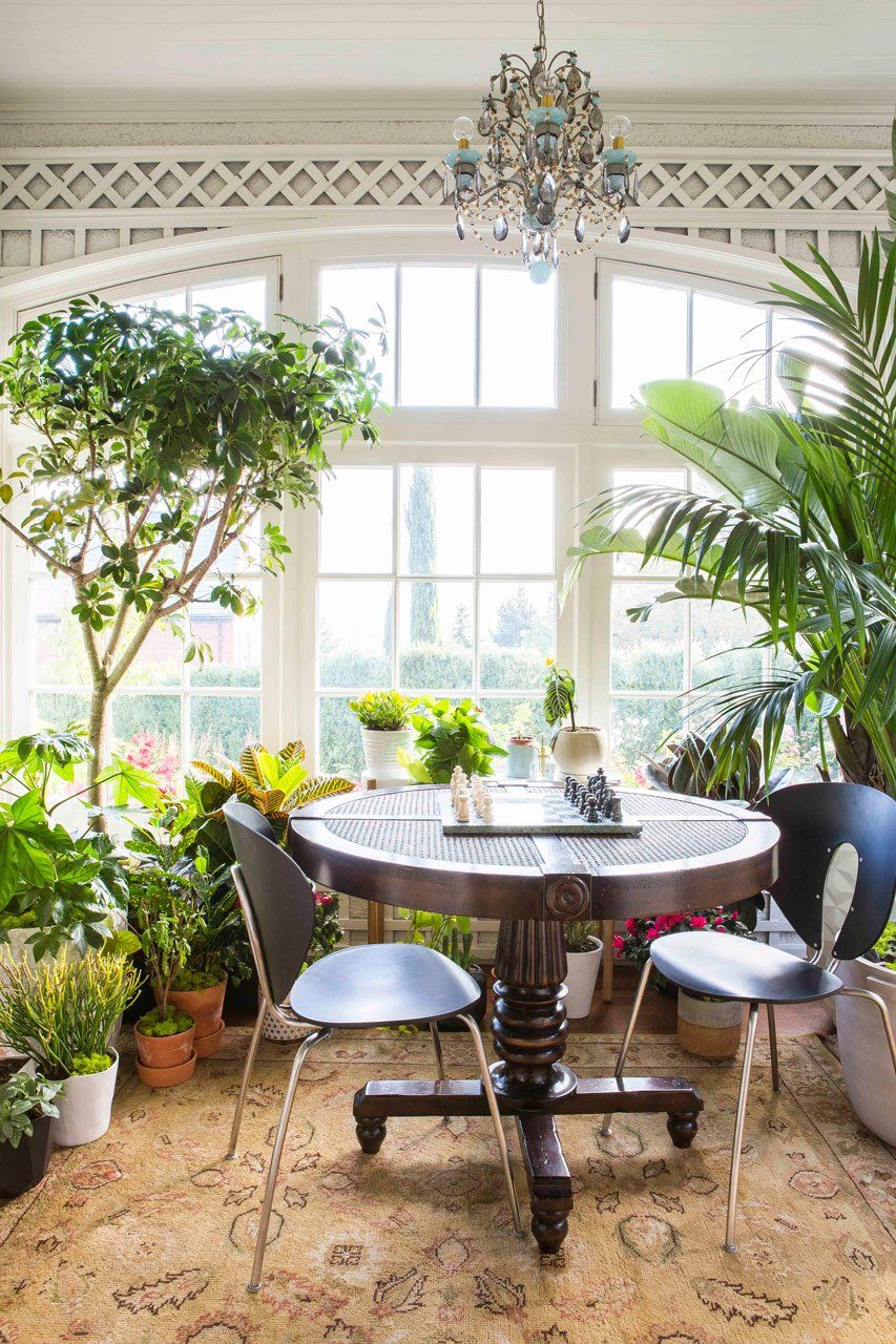 We restored the original 1st floor sunroom, full of plants with a round table under a vintage chandelier.