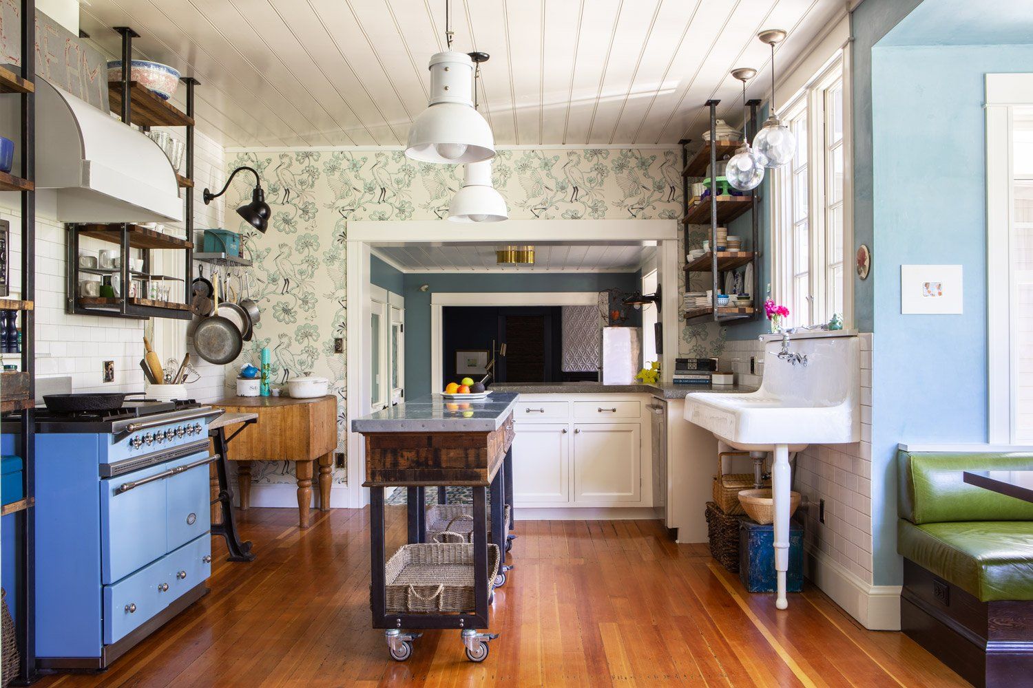 A kitchen with a v-groove ceiling, elegant bird wallpaper, delft blue LaCanche range, salvaged Fir floors, a farm style sink and antiques on open steel and wood shelving.