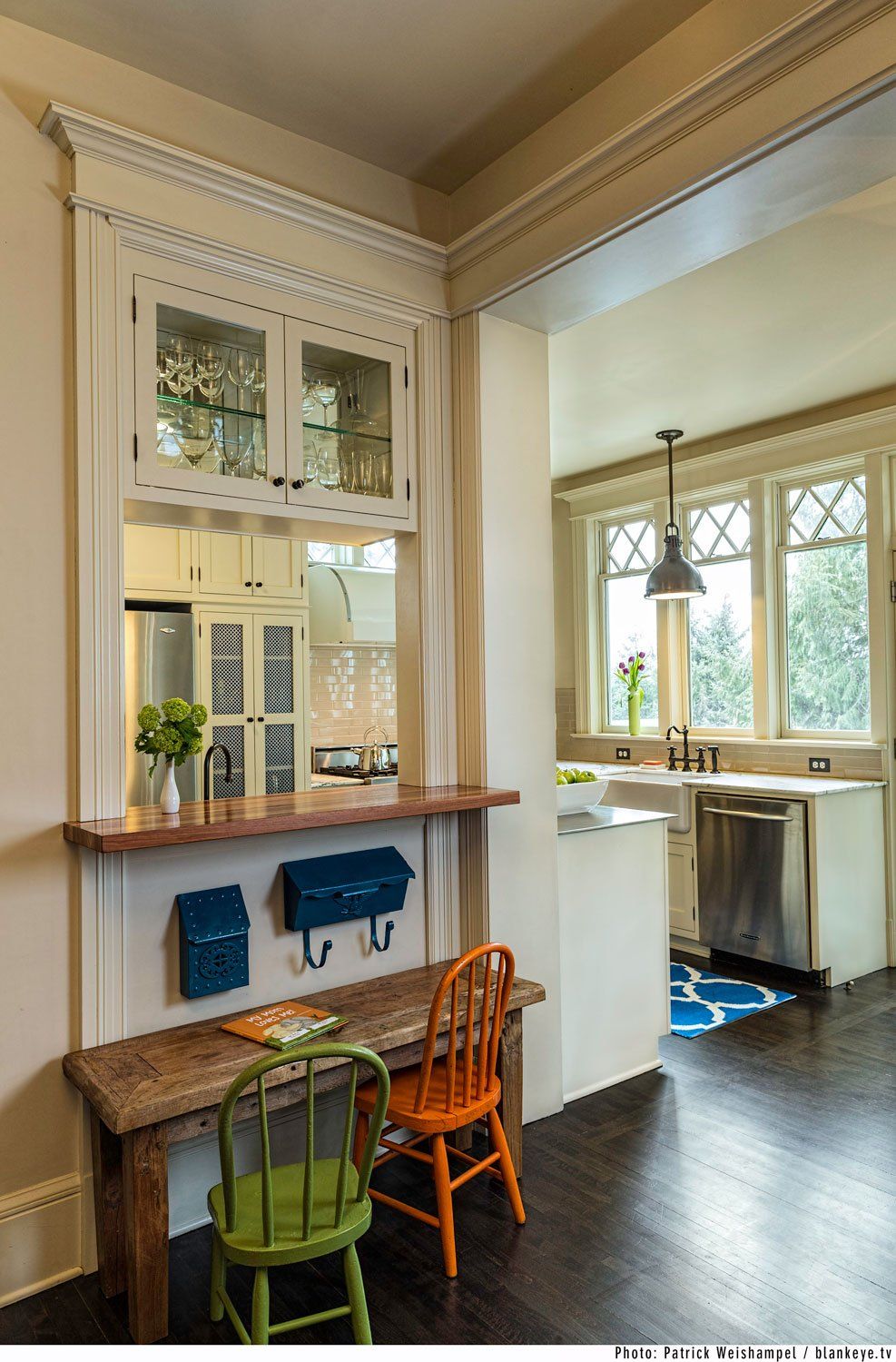 From the informal dining nook you see the family-friendly kitchen with a kids' table, chairs and wall mounted mailboxes under a cased pass-through with display cabinets above.