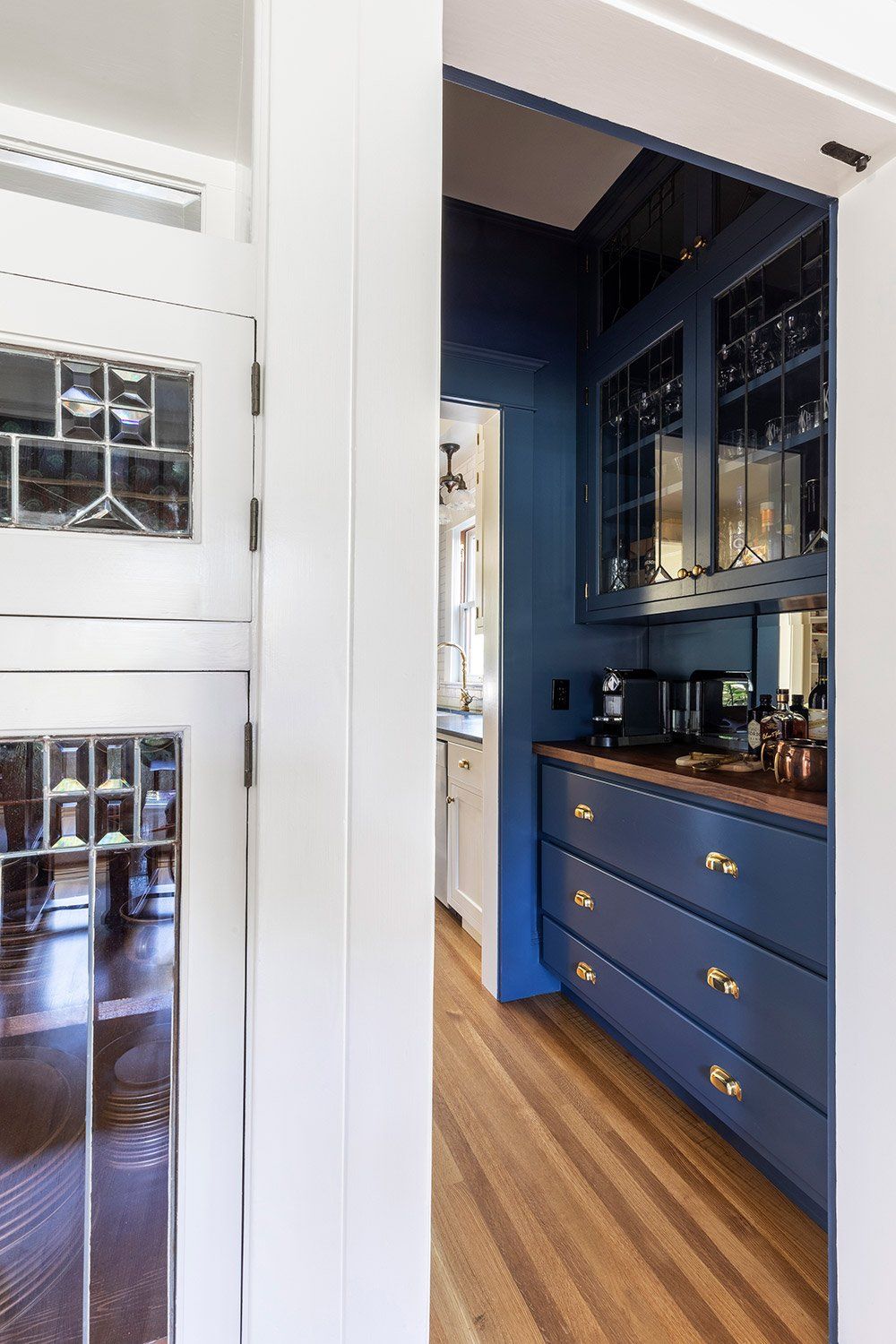 Through the dining room doorway, you see a new pass-through butler’s pantry in a moody blue with barware for entertaining