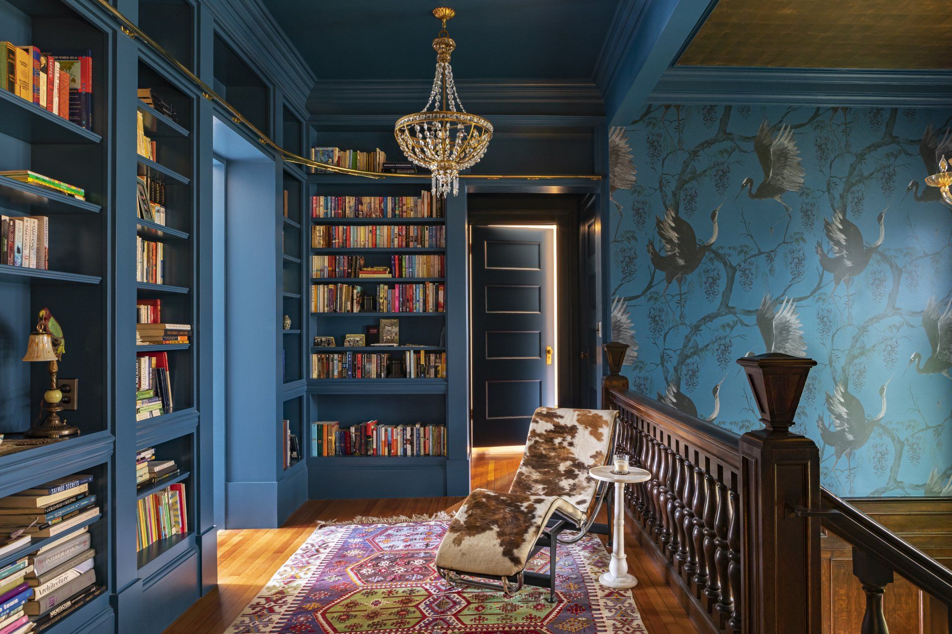 Stair landing with custom library shelving by Arciform, crane Fine & Dandy Co wallpaper and furnished with eclectic fixtures and furnishings.