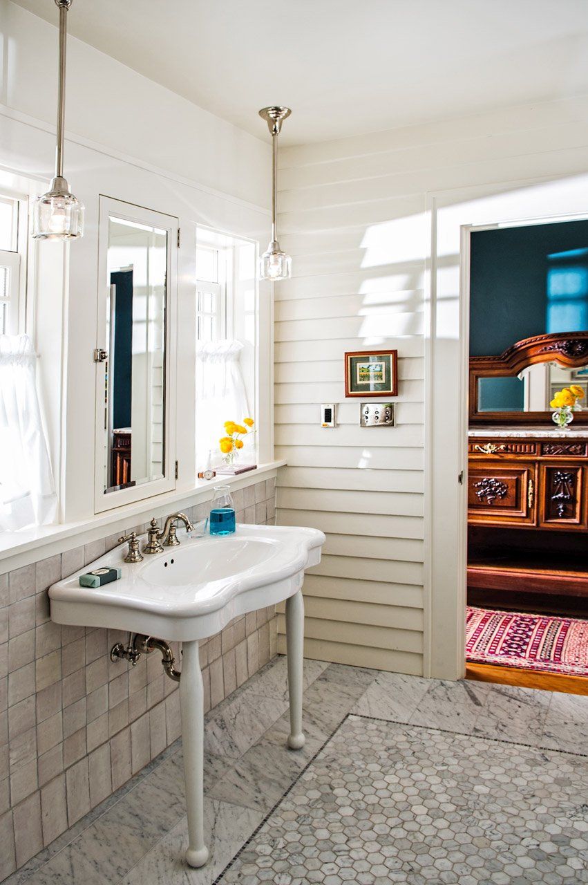 The new main bath has marble tile floors, zellige tiled sink wall and original house siding on the door wall.