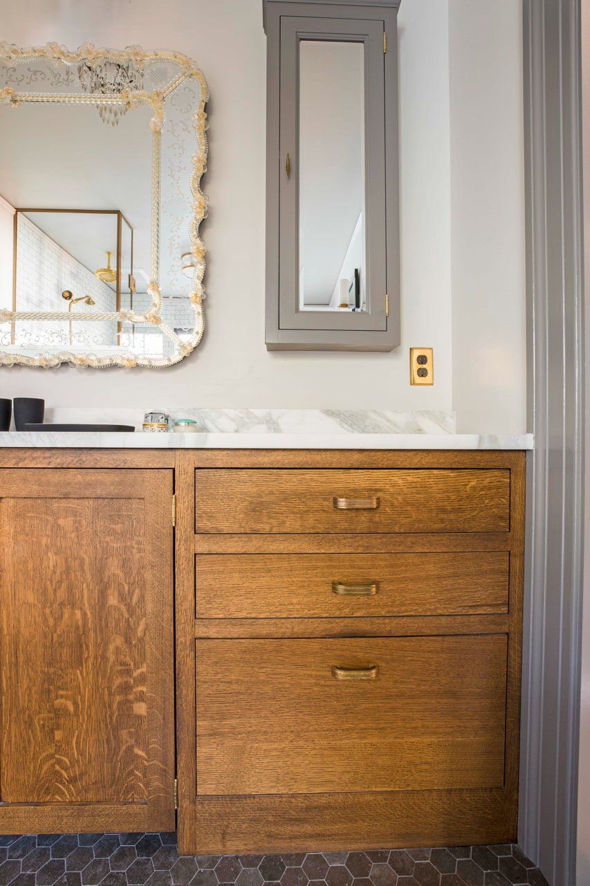 Close up of custom stained vanity cabinet, mirrors and grey stone hex tile in the main bathroom