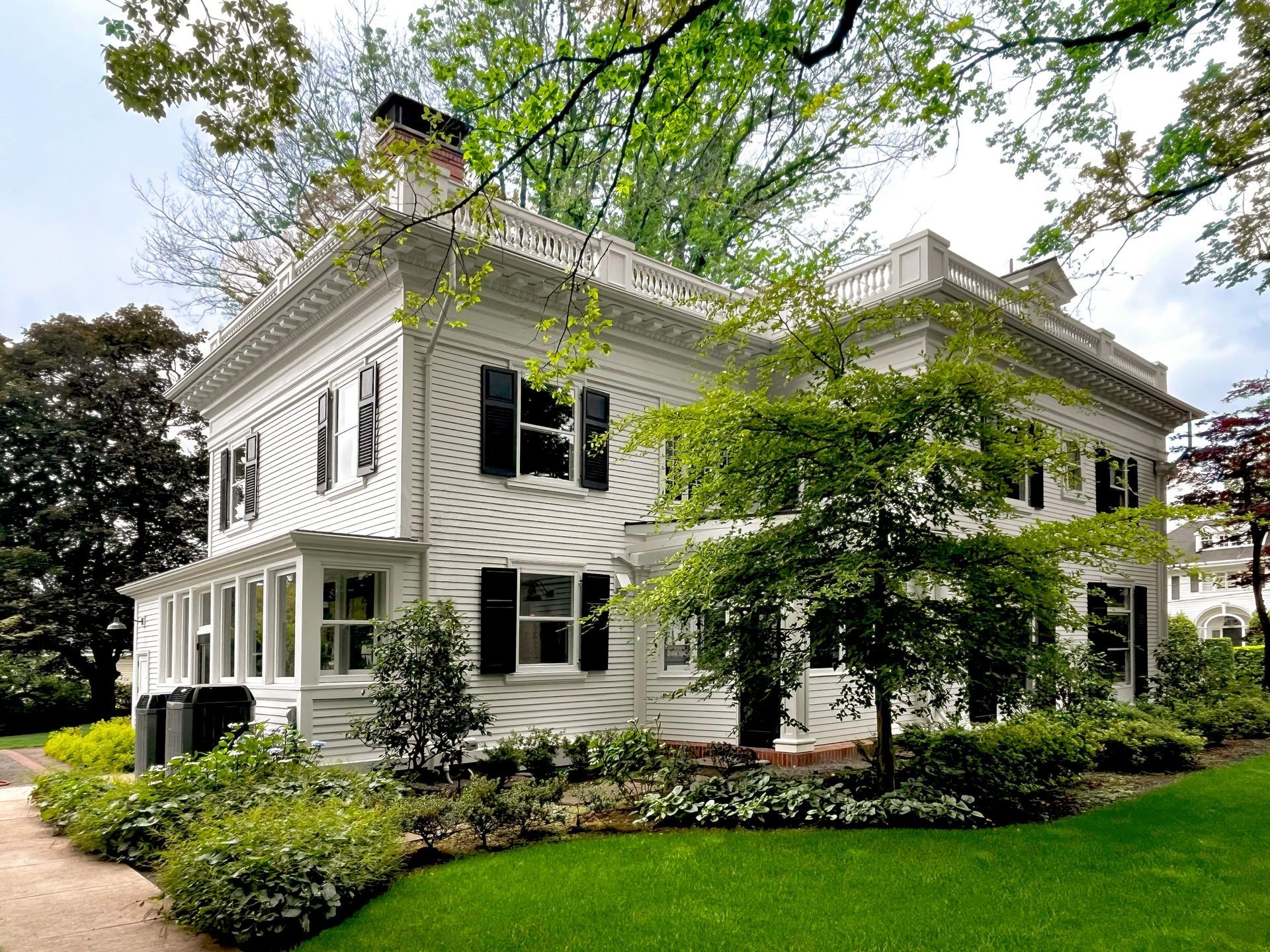 Side and back view of colonial mansion showing, original shutters, restored parapet balustrade, the breezeway entrance, and the sunroom.
