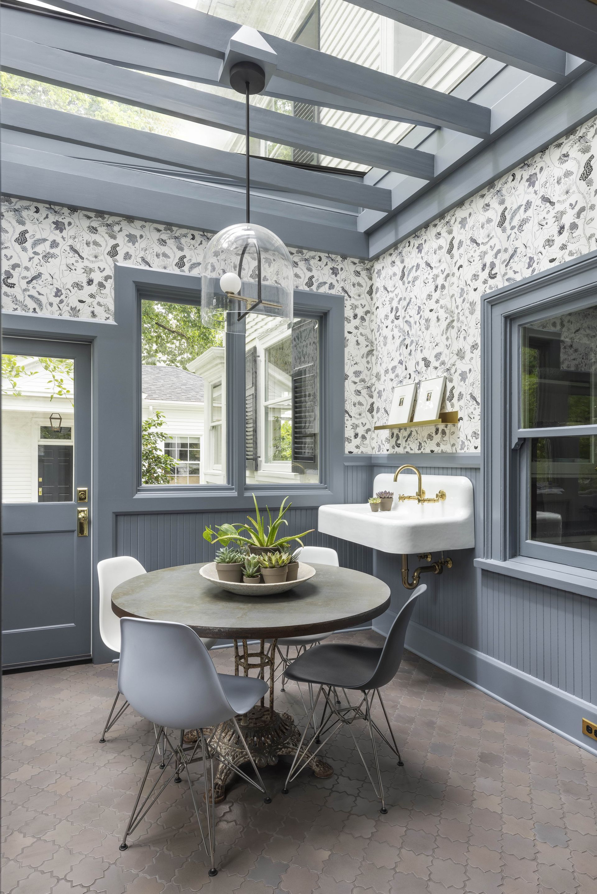 1920’s sunroom with utility sink, arabesque tile floor, floral wallpaper, and vintage French table with Eiffel chairs.