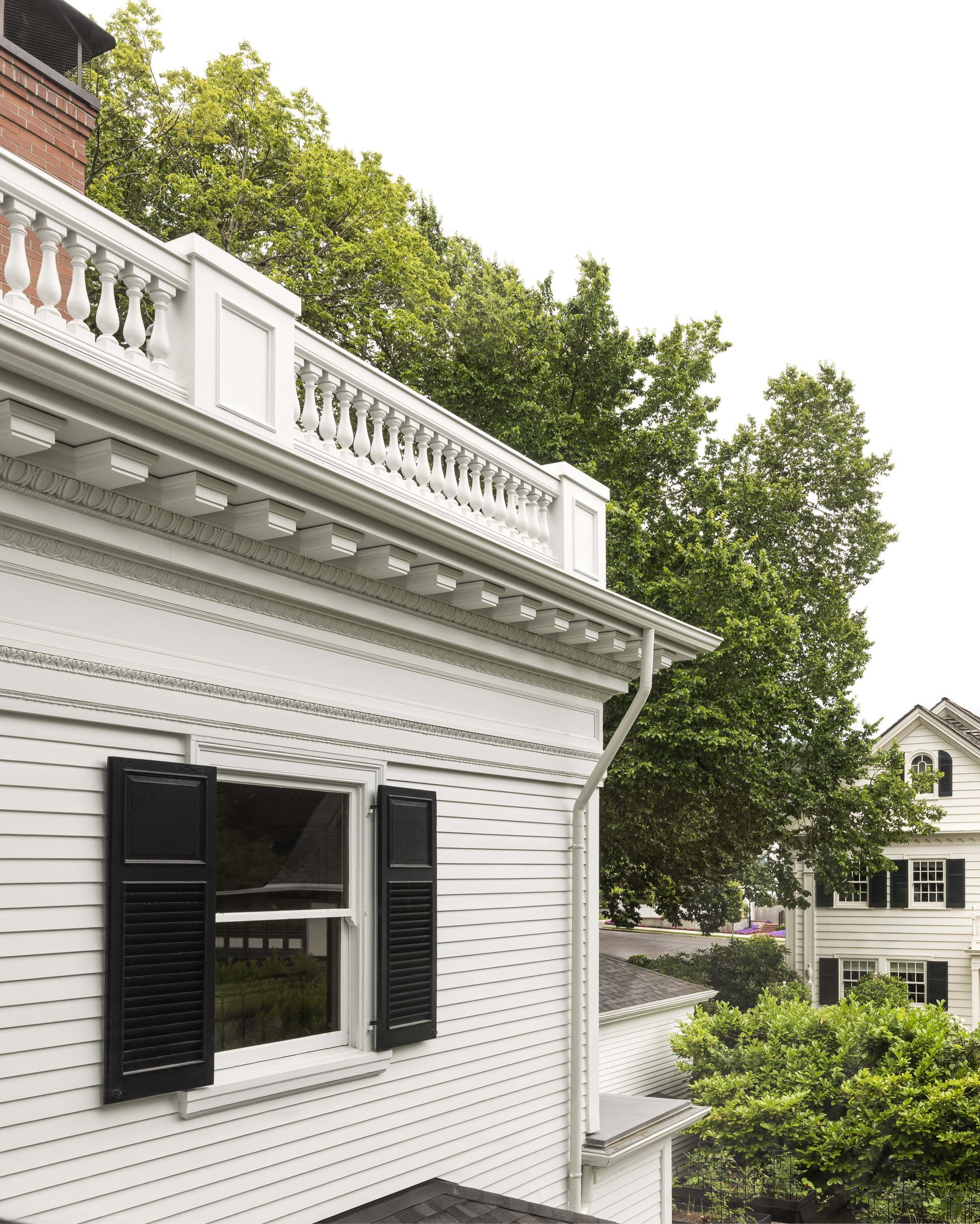 The eave of a colonial mansion showing a restored parapet balustrade, dentils and egg and dart molding details as well as original shutters on a double hung window.