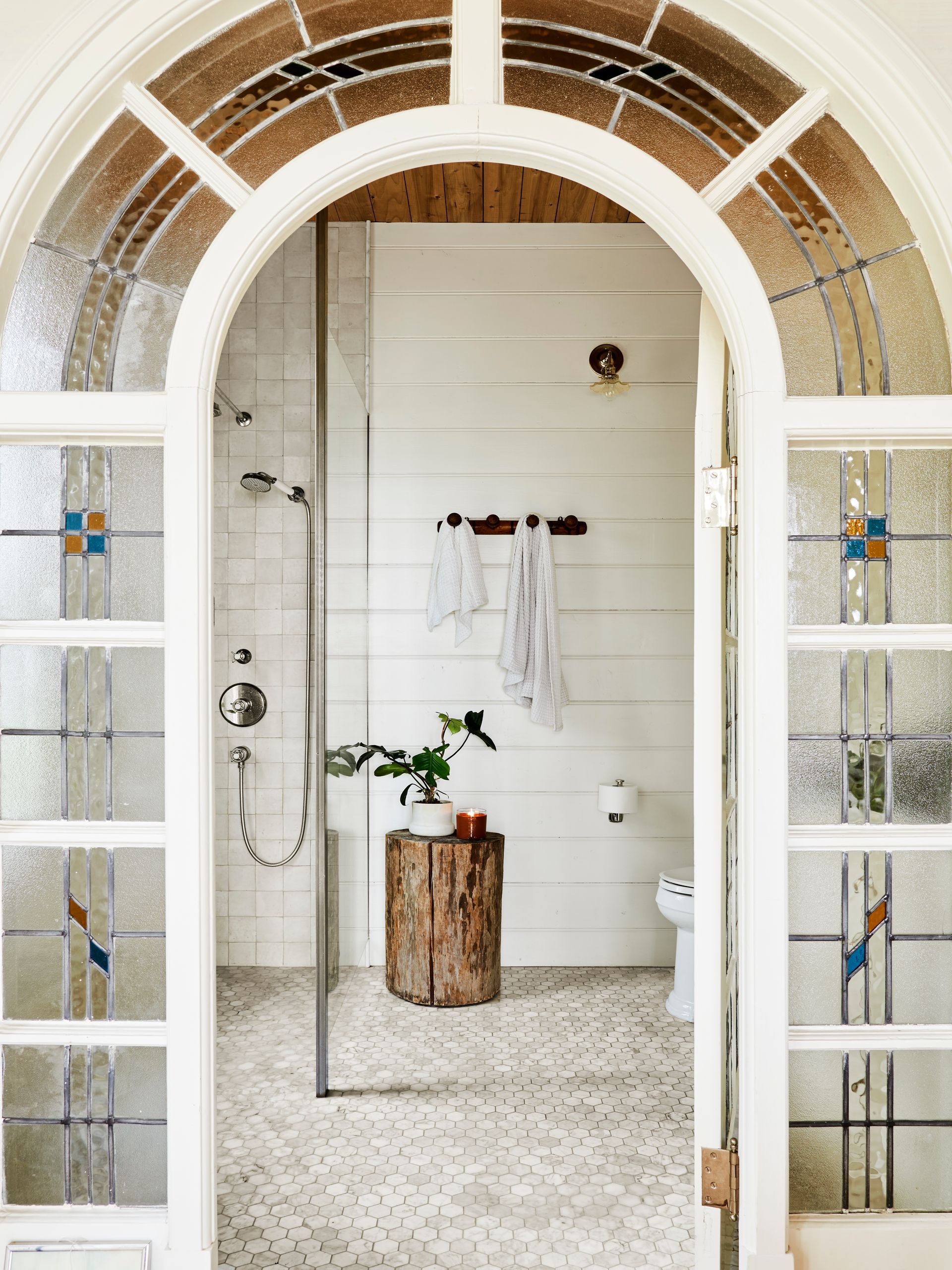 Salvaged leaded-glass, arched door with cottage style bathroom beyond.