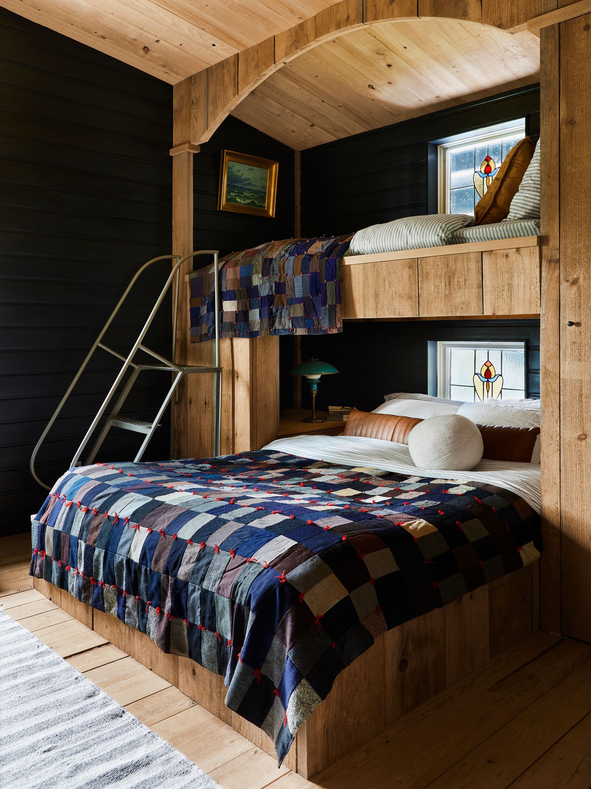 Bunkbed made of rough sawn timber with quilted throws, salvaged stained glass windows and an industrial rolling ladder.