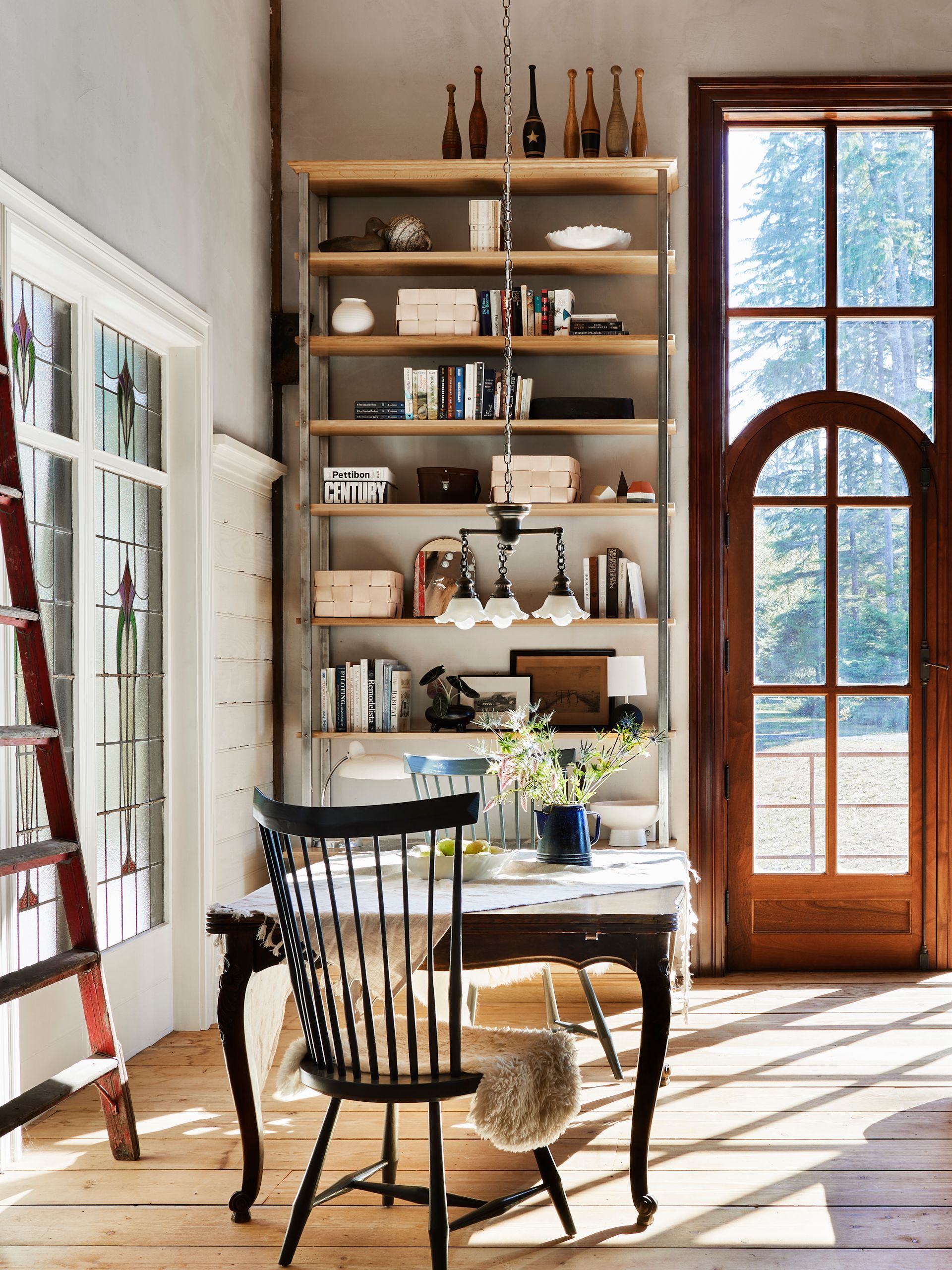 Custom bookshelf and window with integrated door, salvaged stained- glass window, wide plank flooring and eclectic fixtures and furnishings.