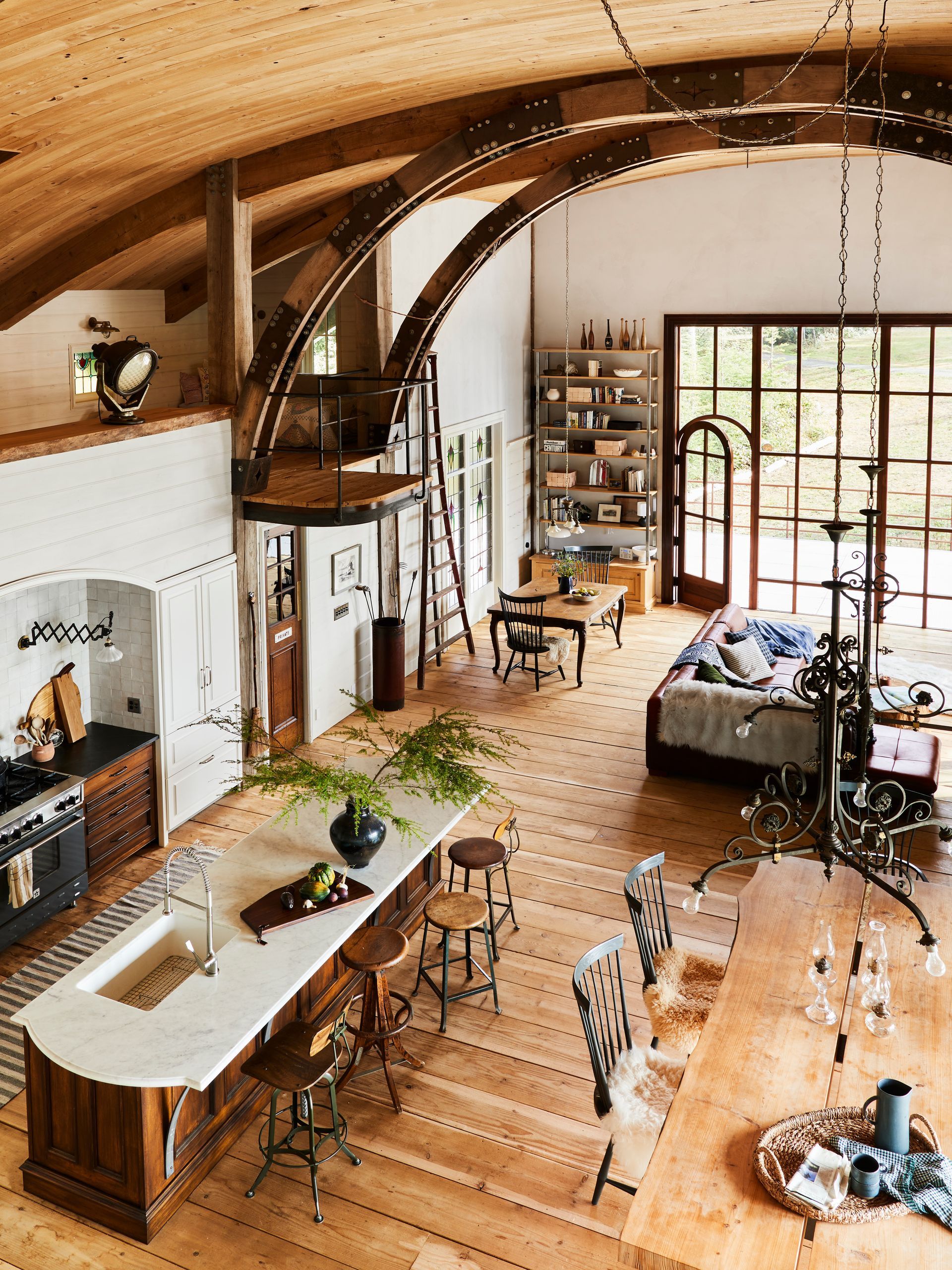 Large, open living space with broad kitchen island, eclectic fixtures and furnishings, and generous custom window with integrated, arched-top door.