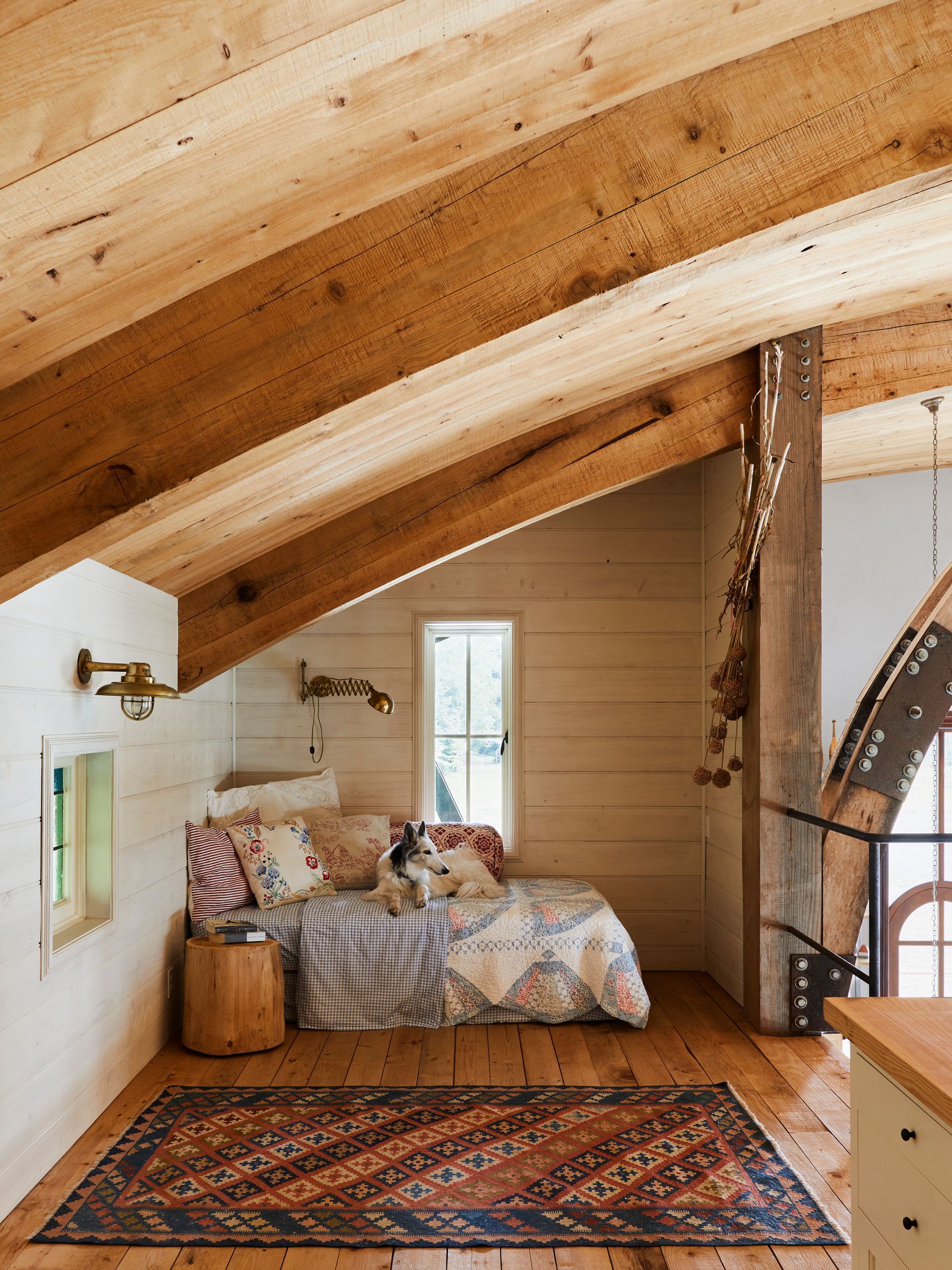 Sleeping loft with barrel ceiling and arched beams, stained paneling on walls and car decking on the floor with nautical lights and a silken wind hound dog on daybed.
