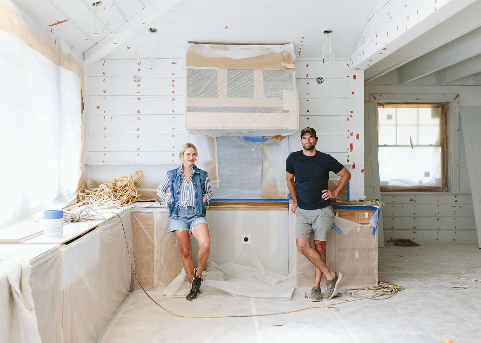 A man and a woman are standing in a kitchen under construction.