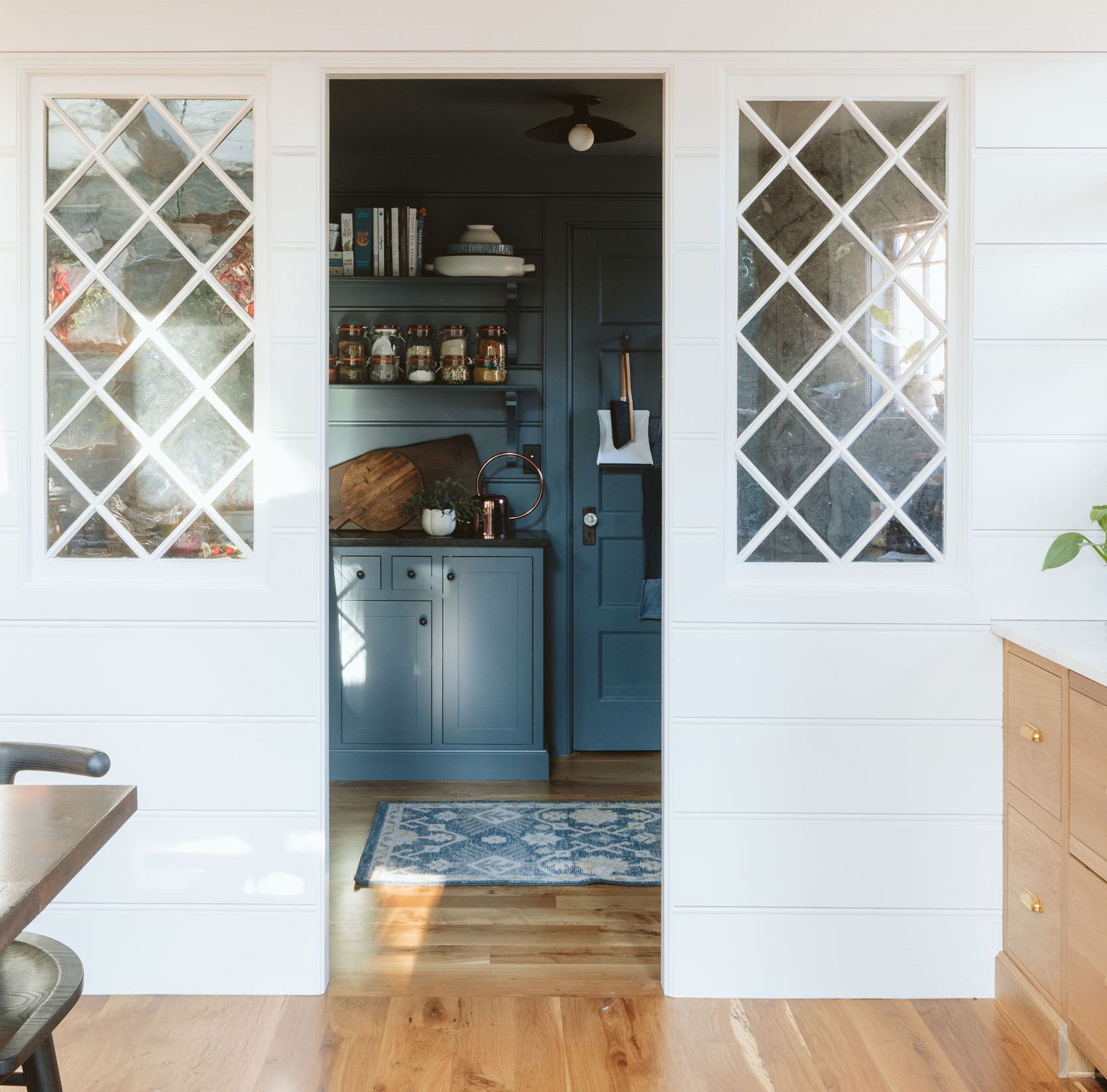 A whole house remodel of this 1910 SW Portland farmhouse included the creation of a dedicated walk-in pantry/side entry. Internal diamond pane windows are a charming way to connect the spaces visually and bring light into the contrasting moody interior.