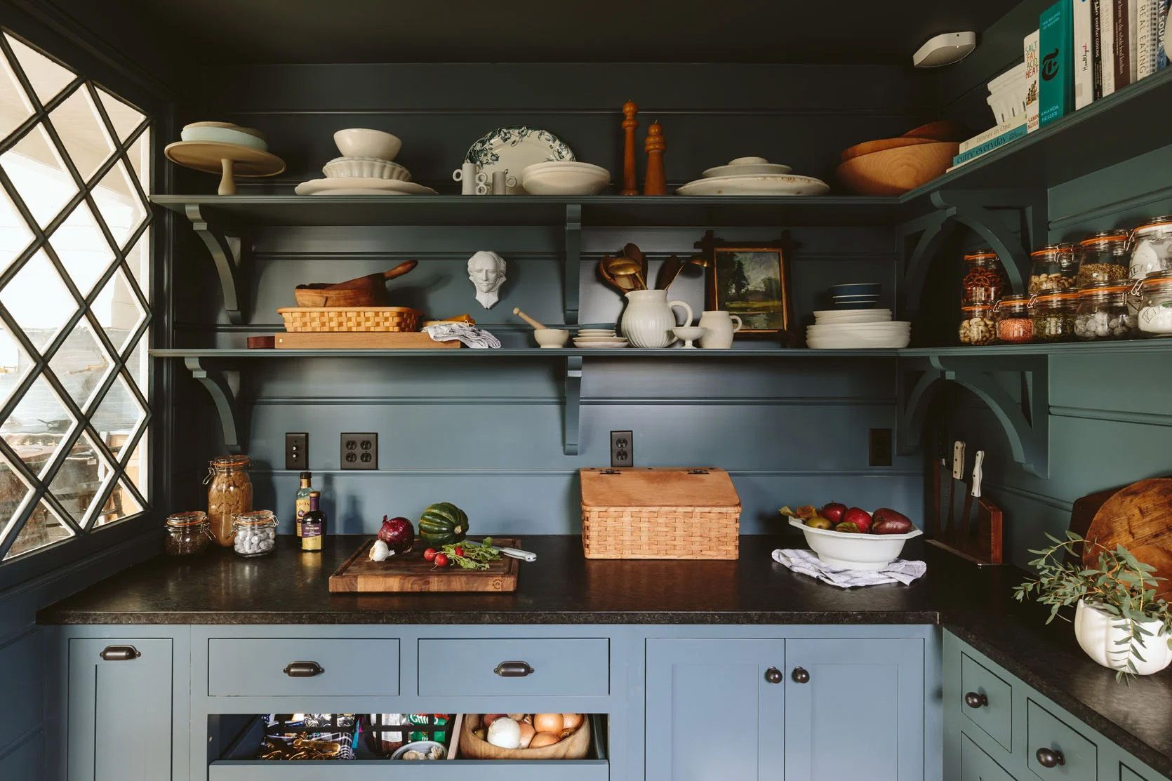 Tongue-and-groove board walls and two tiers of open wood shelving reinforce the turn of the century farmhouse look. The moody dark paint creates a cozy contrast with the adjacent bright-white kitchen. 