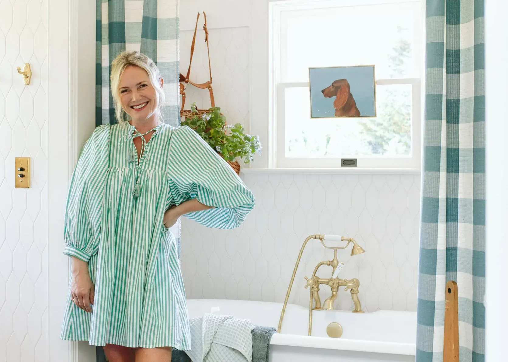 A woman in a green dress is standing in a bathroom next to a bathtub.