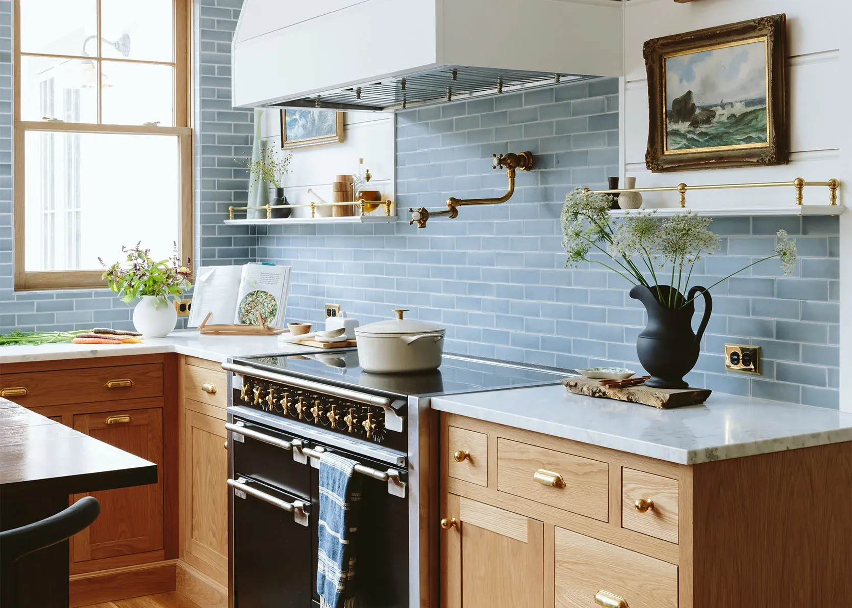 A kitchen with blue tiles , wooden cabinets , a black stove and a painting on the wall.