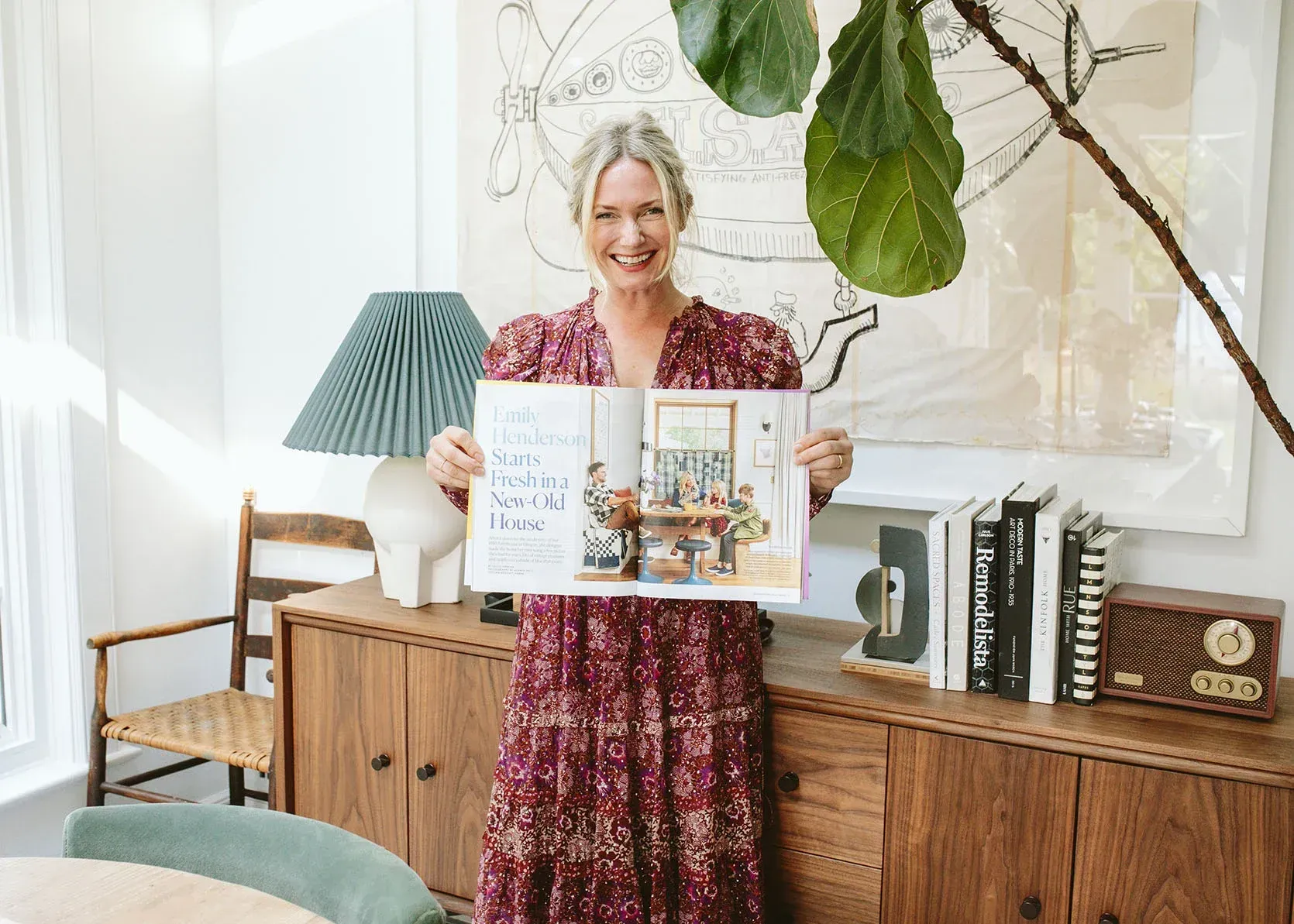 A woman in a red dress is holding a book in a living room.