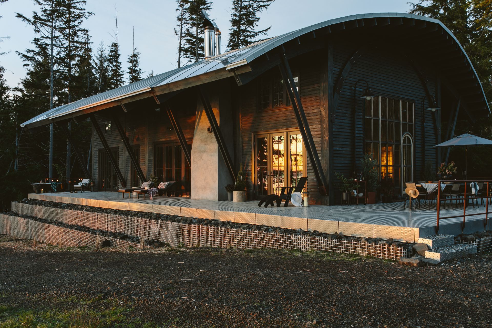 Barn-like custom home with barrel roof, black stained lap siding, and gabion wall.
