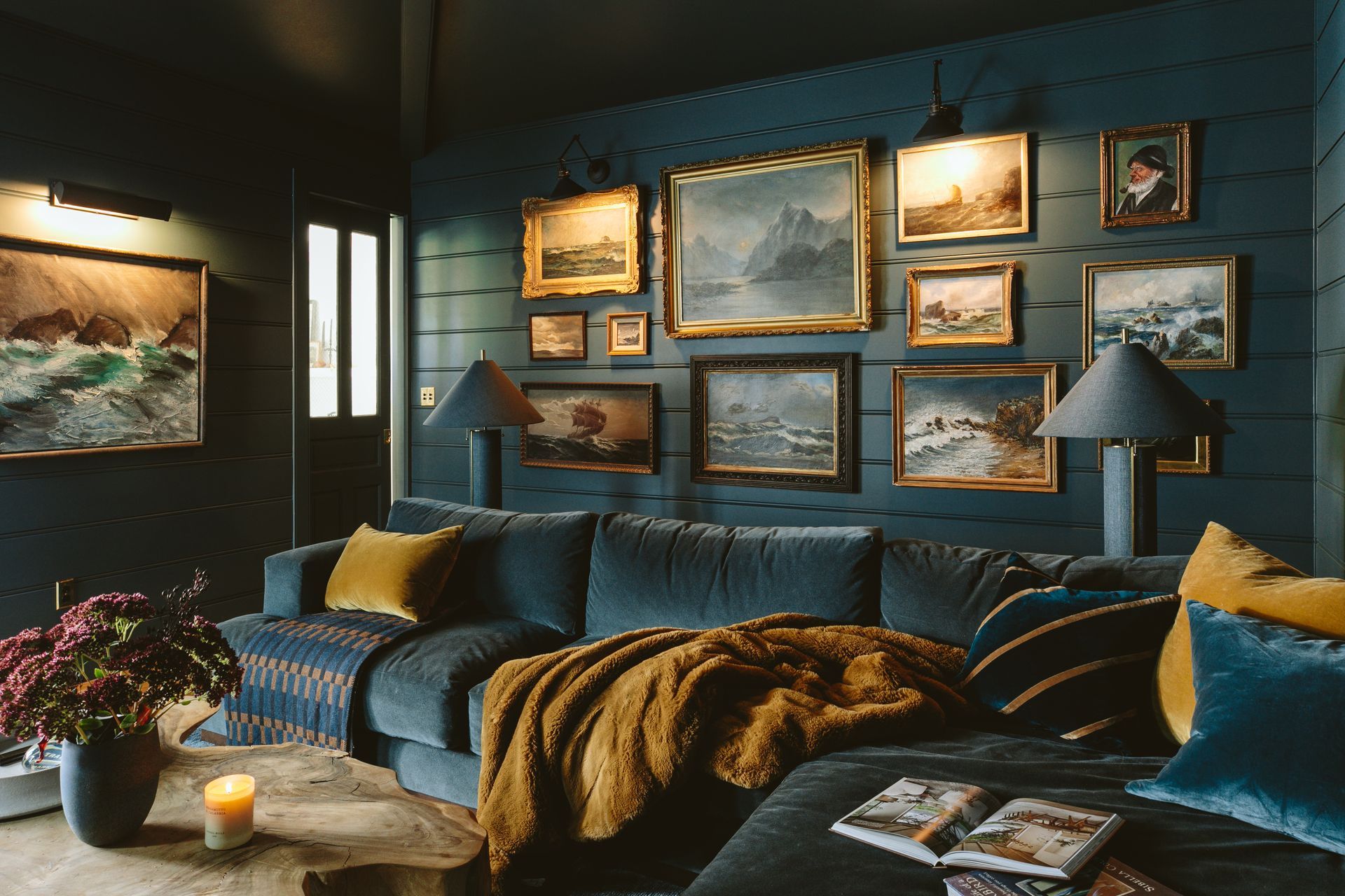 The deep blue den features an dark blue velvet sectional with ochre pillows and throws. Vintage seascapes adorn the beadboard paneled walls.