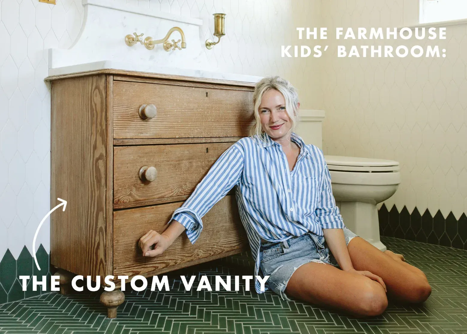 A woman is sitting on the floor next to a dresser in a bathroom.