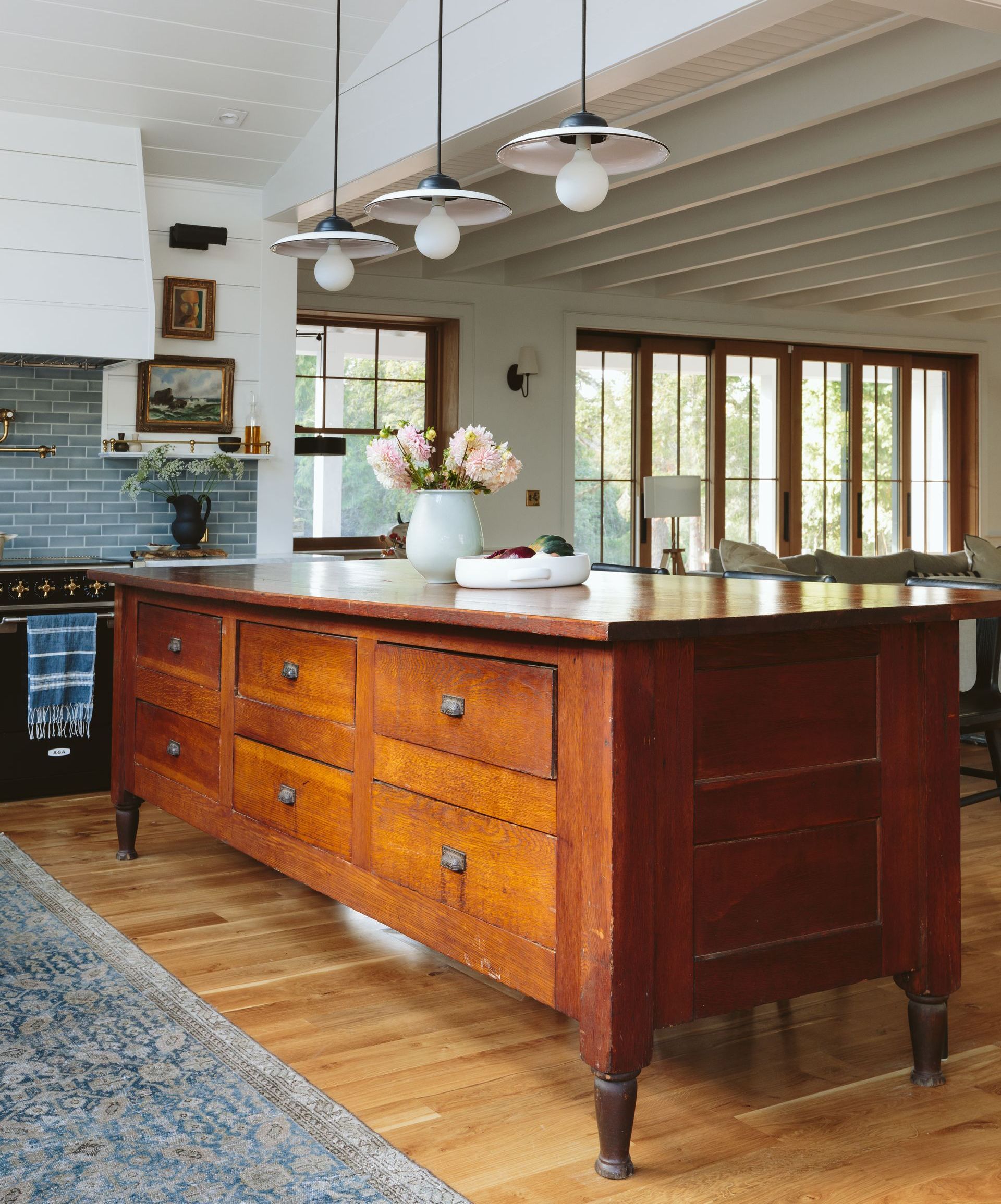 A refurbished vintage cabinet functions as kitchen island, lit by industrial style pendants with the living room in the background.