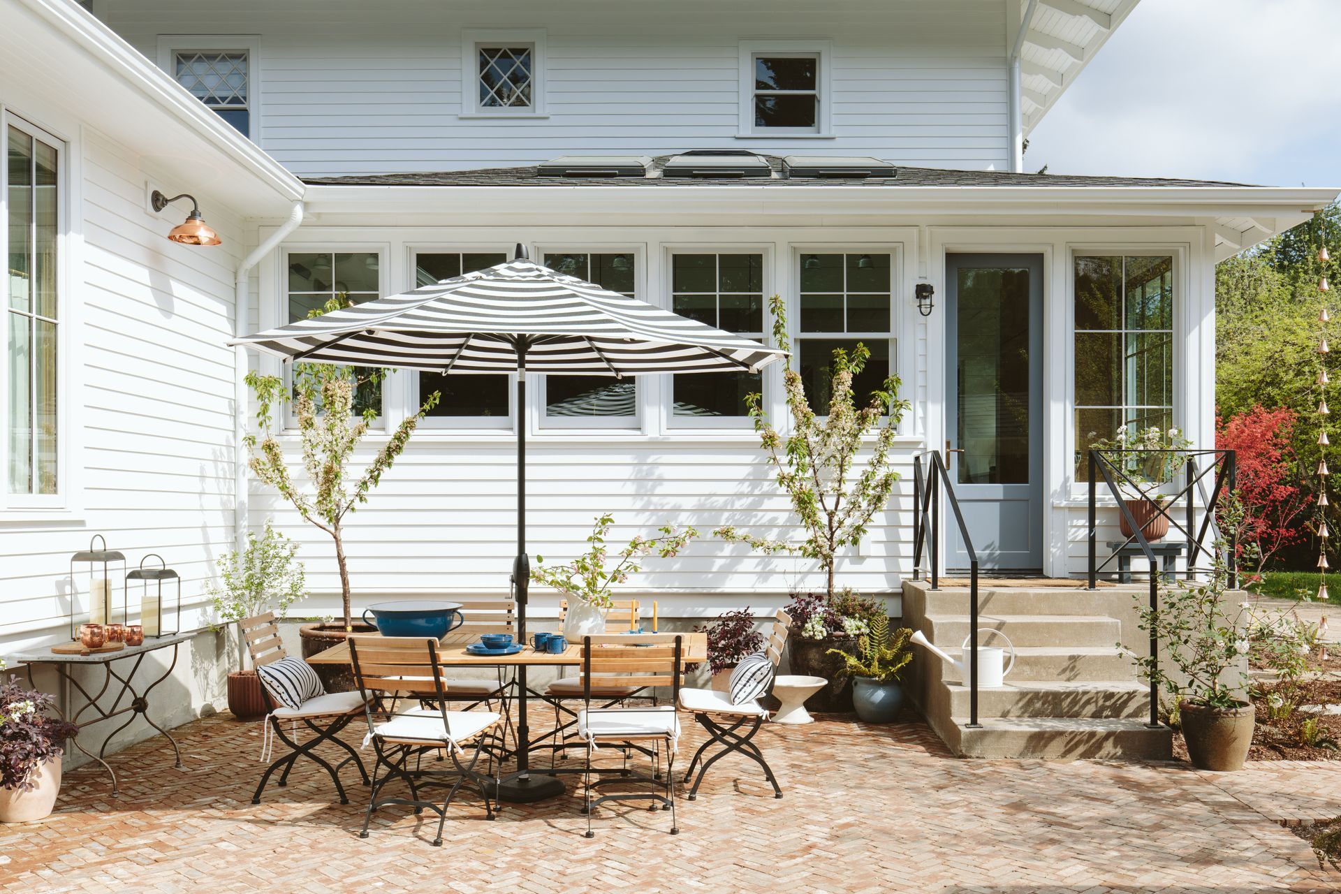 Remodeled 1960’s addition behind a 1910 farmhouse with concrete landing and steps leading to a brick paved patio with outdoor dining set and striped sun umbrella.