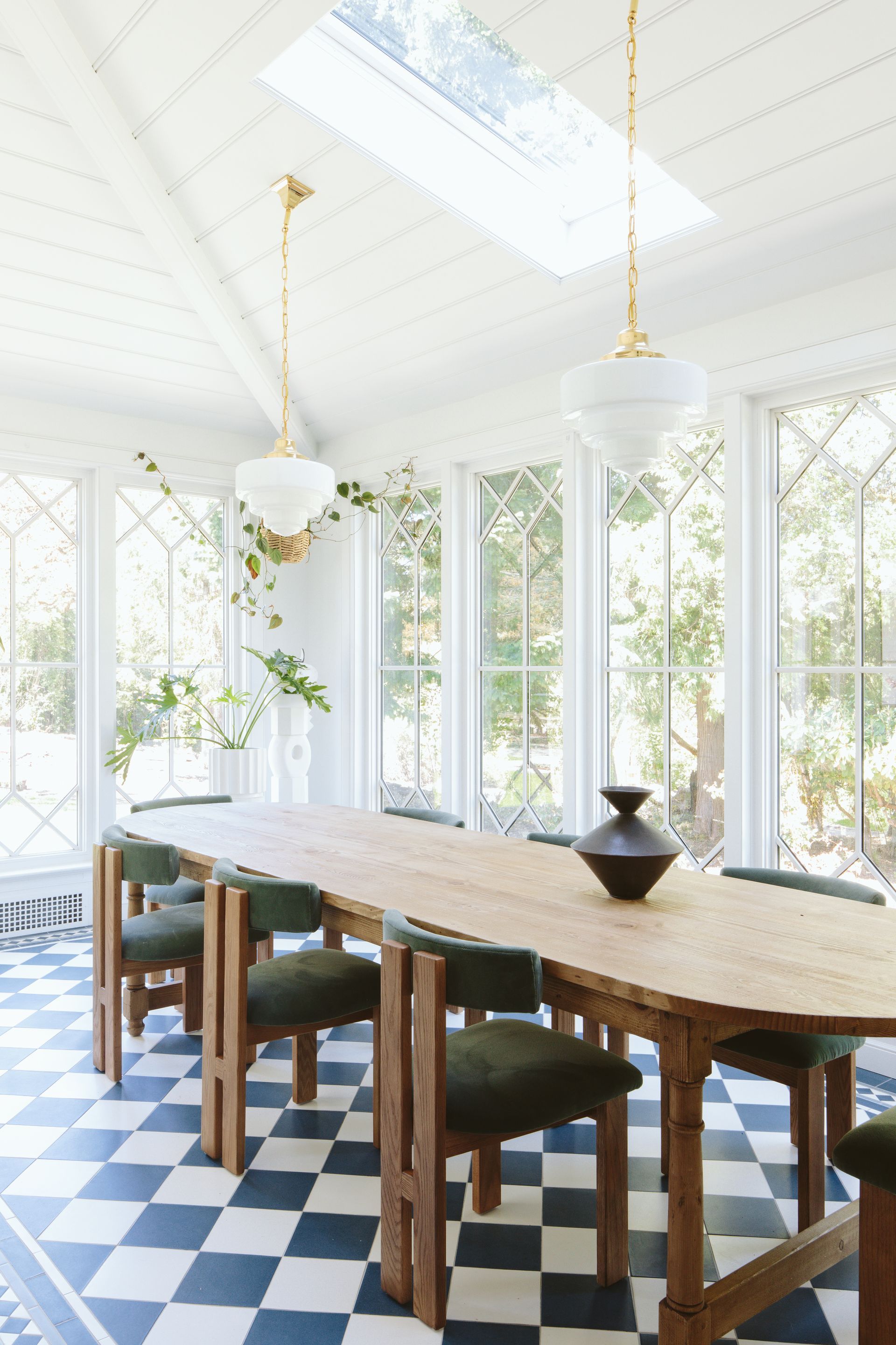 Sunroom with blue and white checkered tile floor with border, large windows with diamond shaped lites, vaulted ceiling with skylight and schoolhouse pendants, contemporary dining chairs and a  vintage table.