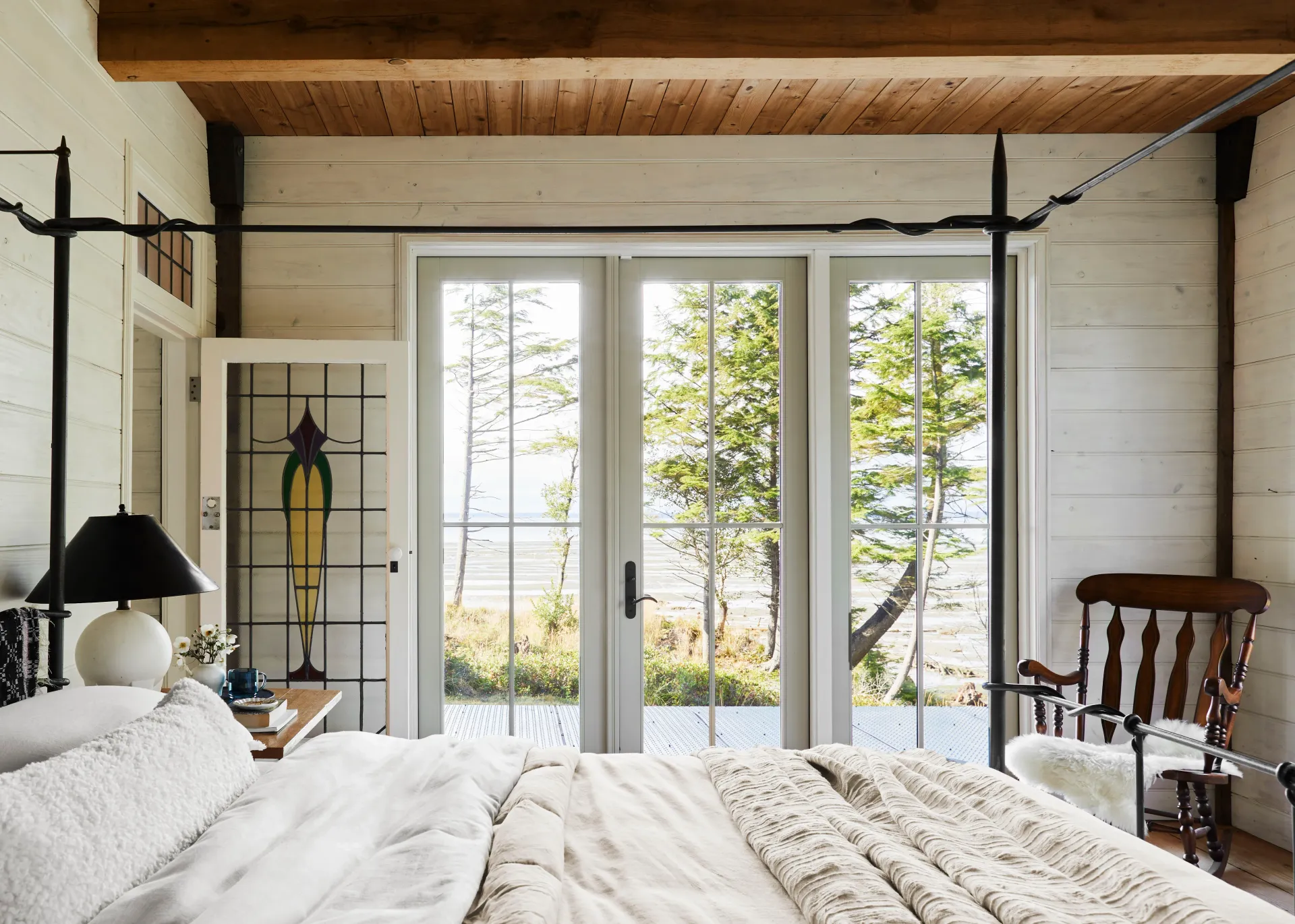 A bedroom with a canopy bed , chair and sliding glass doors.