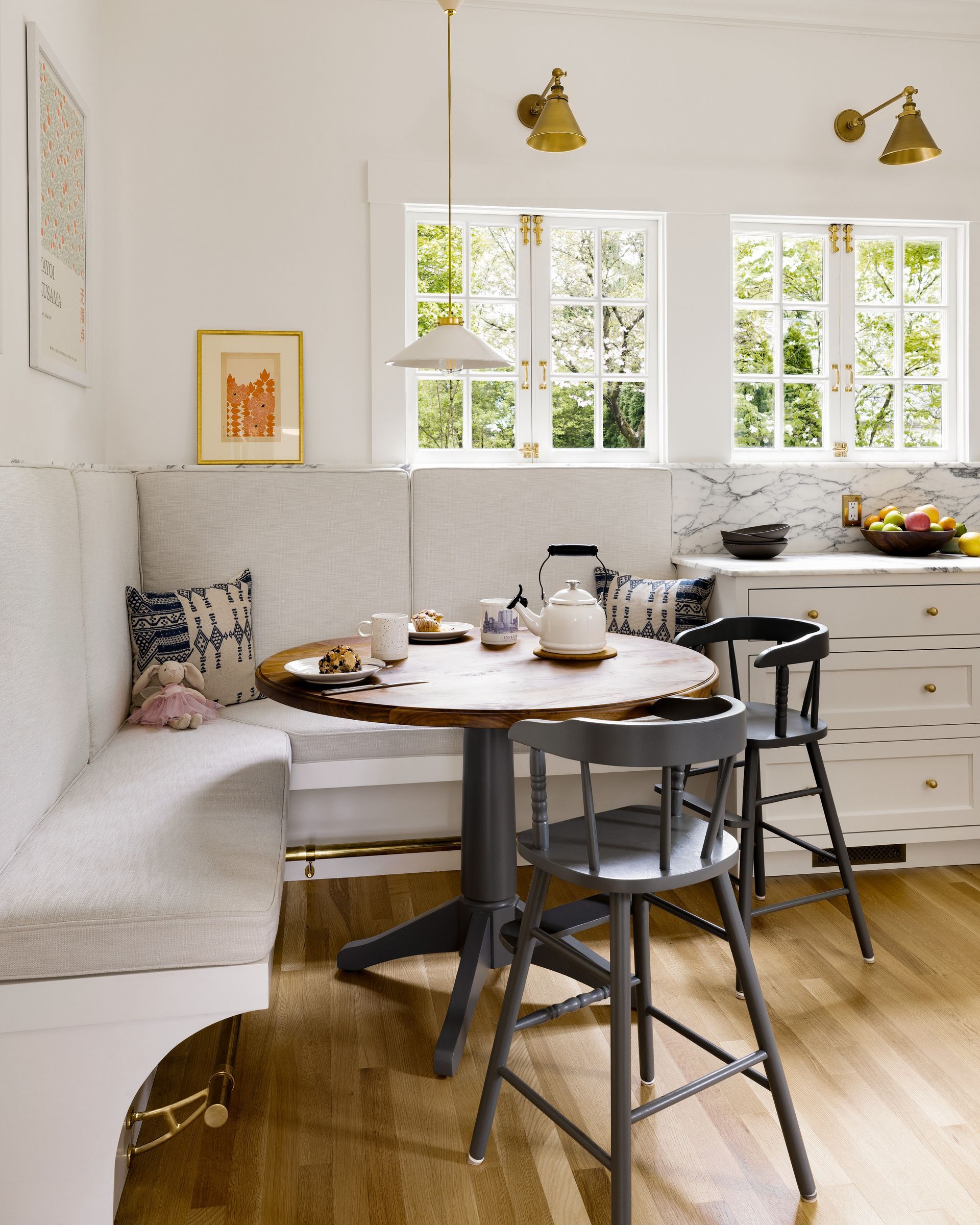 At the end of the sink wall cabinet run is a corner banquette with a brass footrail and upholstered bench, round table and a pendant to light up the table on short winter days.