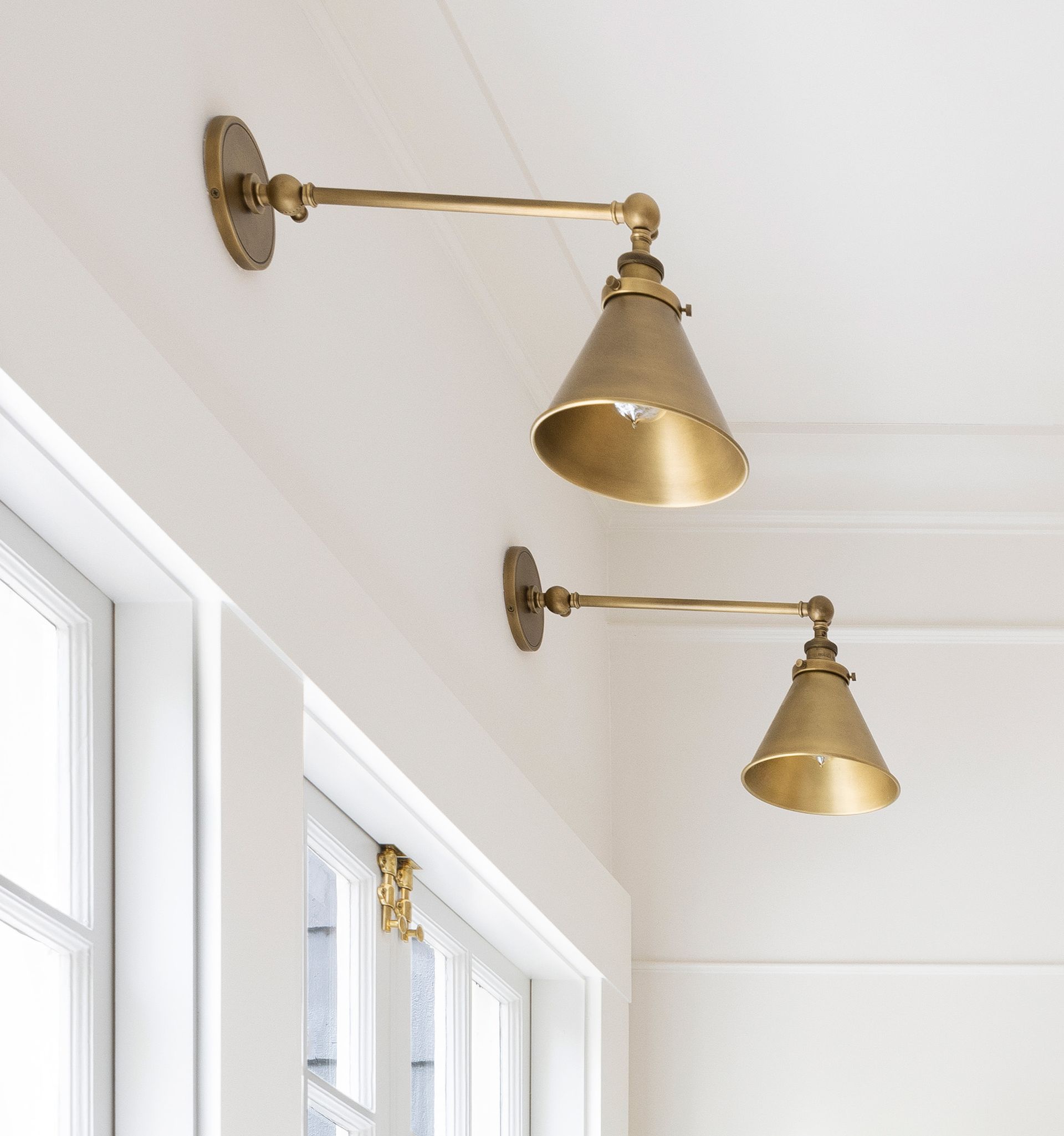 Above the two windows are two unlacquered brass library sconces with cone shaped shades for a warm glow.
