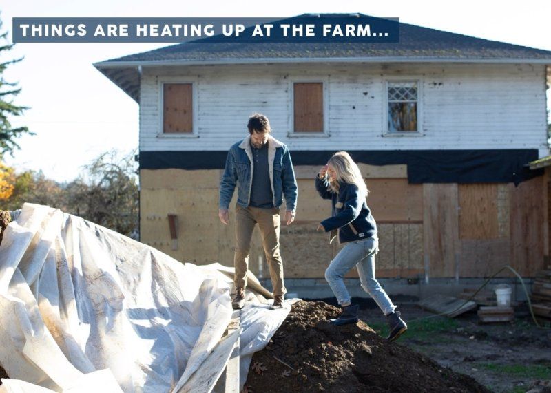 A man and a woman are standing on a pile of dirt in front of a house with the words things are heating up at the farm