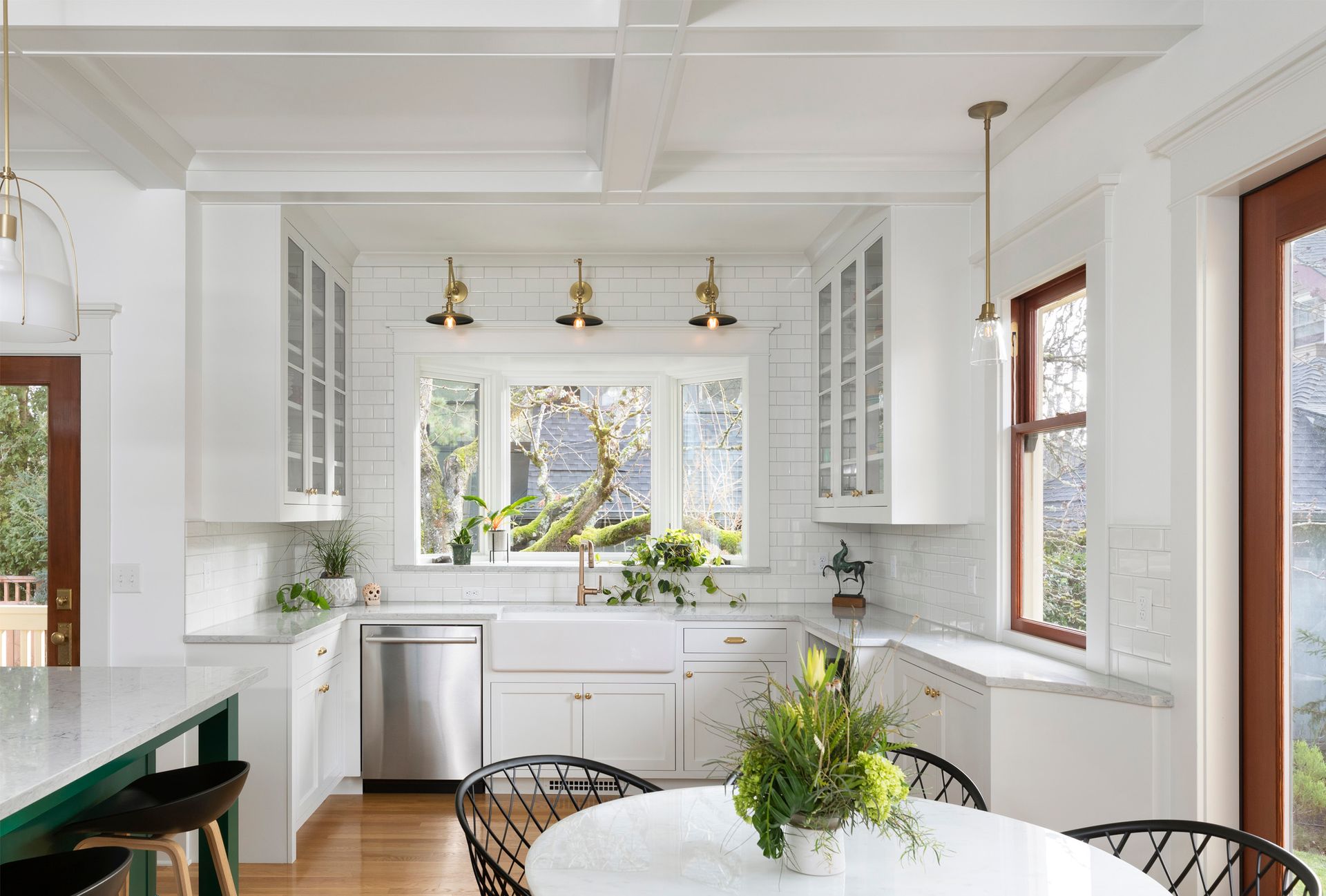 Airy dish washing alcove in a 1910’s style kitchen remodel with apron sink, brass sconces and a contemporary dining set. 
