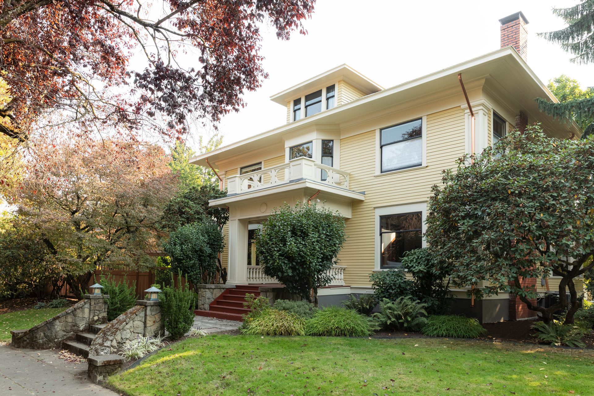 Pale yellow Craftsman Foursquare with distinctive rail around porch balcony roof. 