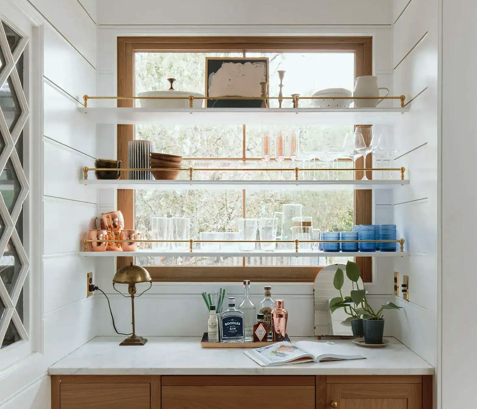 Simple white shelving with a delicate brass gallery rail fills the window alcove in a 1910 Portland farmhouse kitchen.