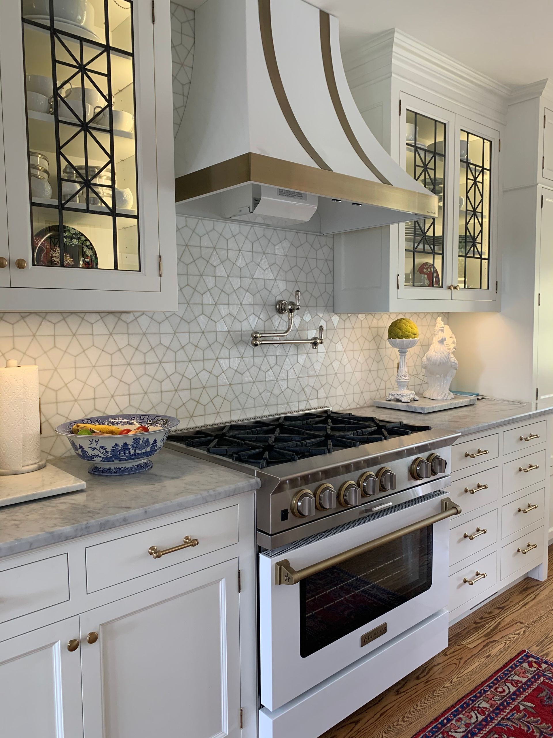 Closeup of  custom white cabinets, backsplash, custom range hood and white gas range.