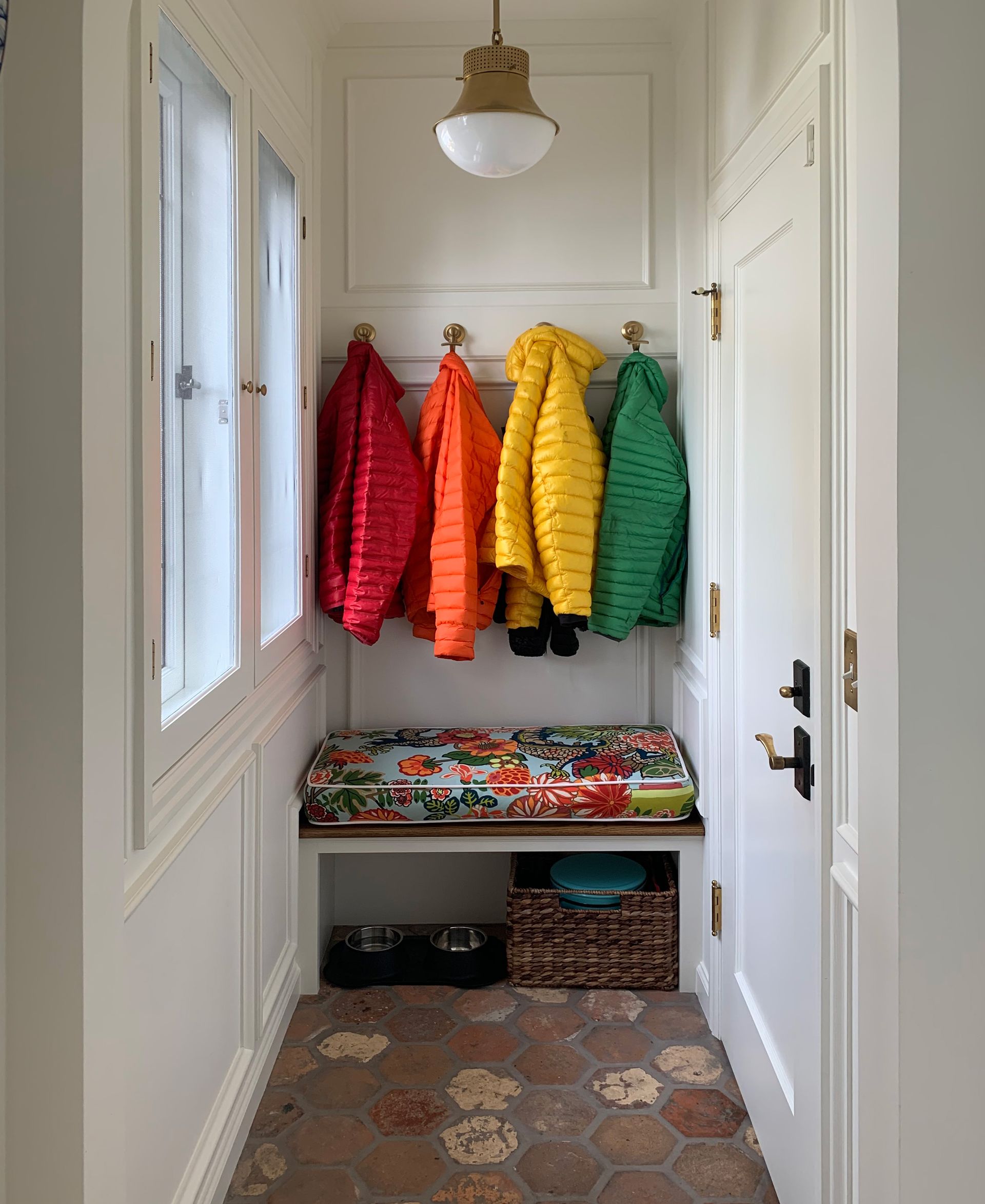 Linking the garage and patio to the kitchen, this mudroom charms with a leaded glass window, cushioned bench and reclaimed terracotta tile floor.