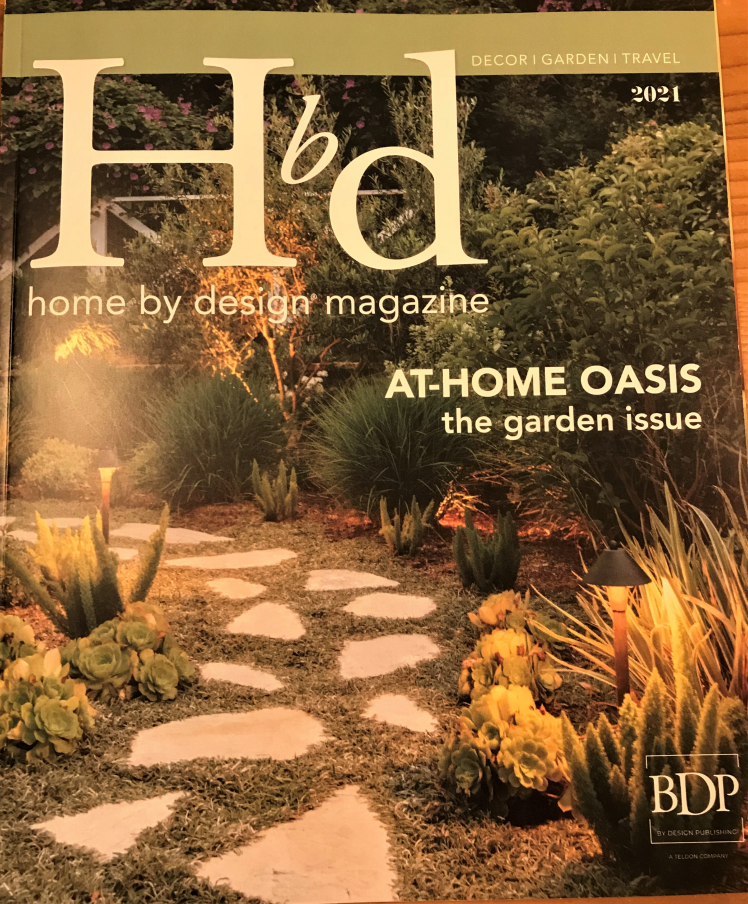 A home by design magazine is sitting on a wooden table.