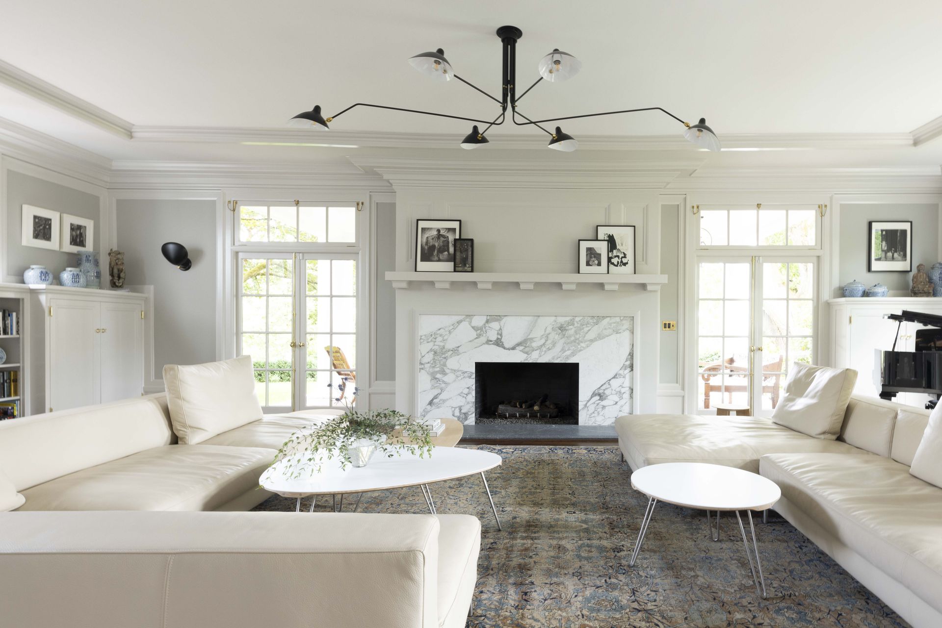 Colonial living room with doors to a covered porch, new stone slab fireplace surround and hearth, a Serge Mouille ceiling light, and roomy comfortable sectionals.
