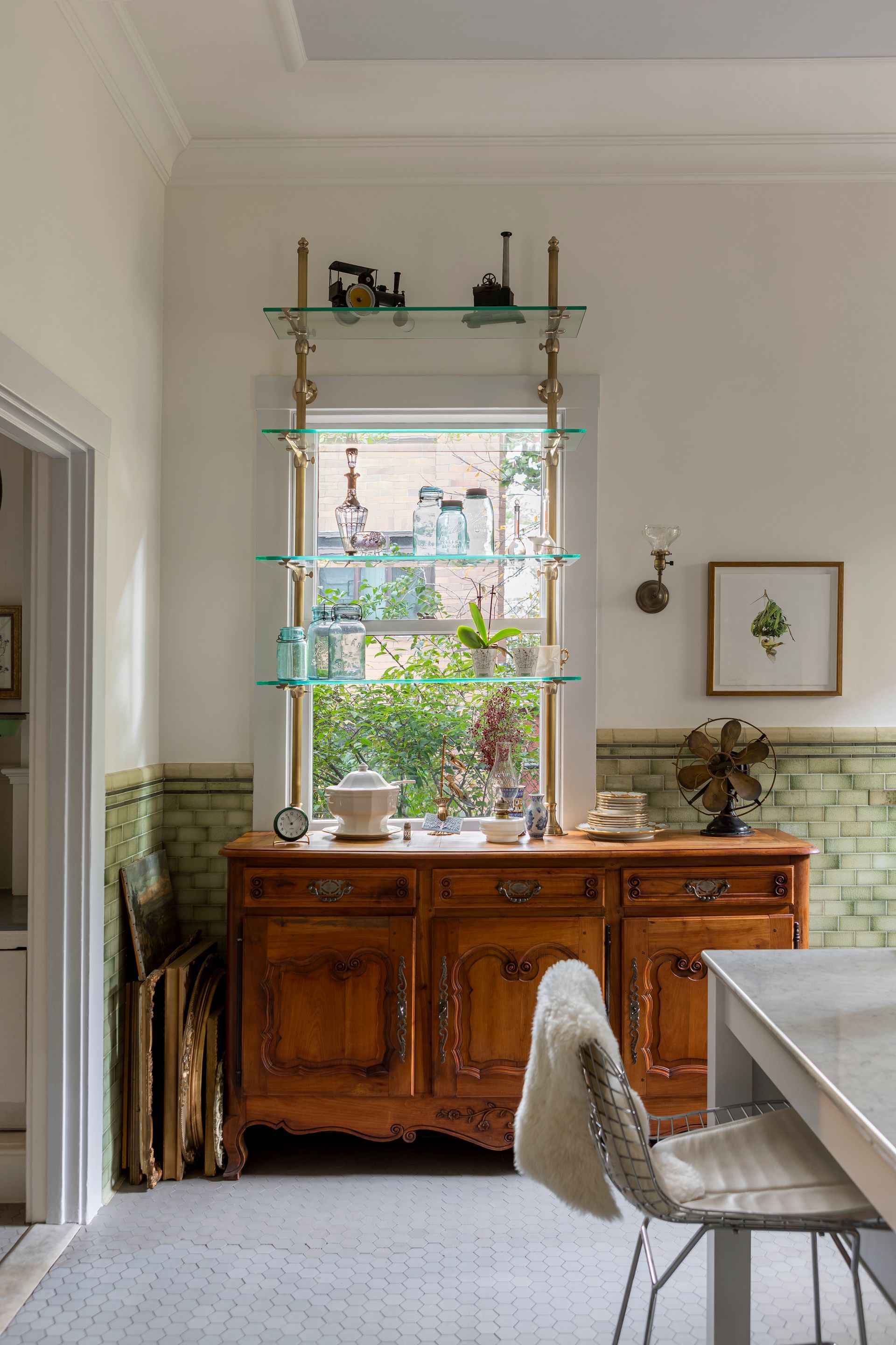 Kitchen corner with French antique buffet cabinet and French bistro shelving in front of window, original wall and floor tile and eclectic decorations.
