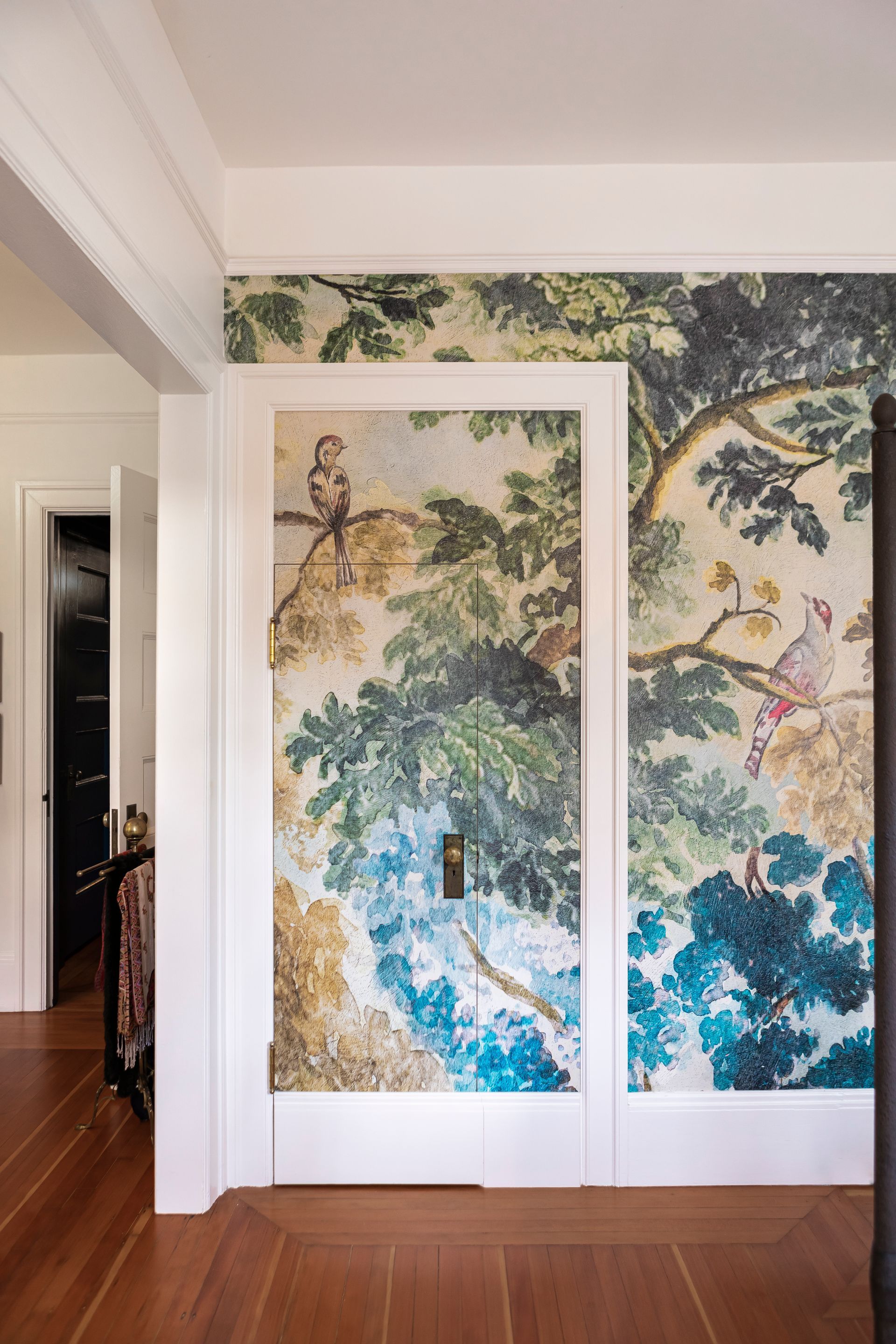 A hidden closet door within a large, cased opening camouflaged by a wallpaper mural.