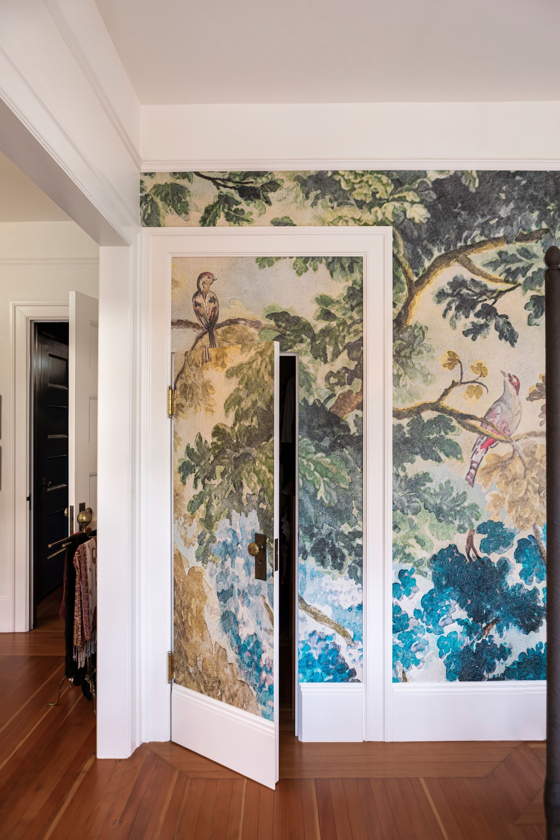 A hidden closet door, ajar, within a large, cased opening camouflaged by a wallpaper mural.