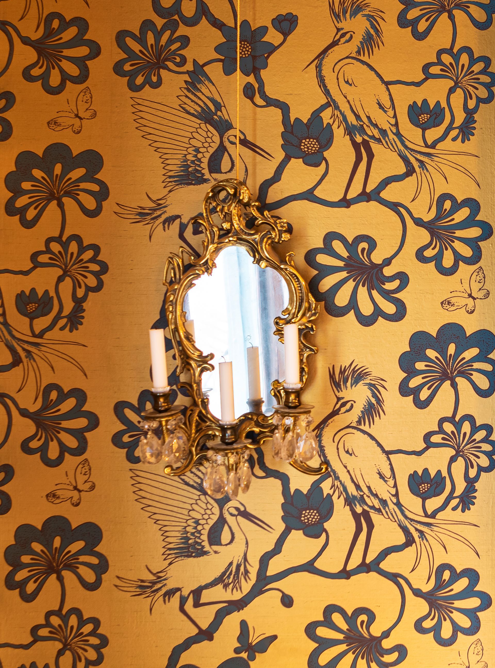 Gold and dark teal Florence Broadhurst wallpaper featuring cranes  with vintage candelabra mirror.