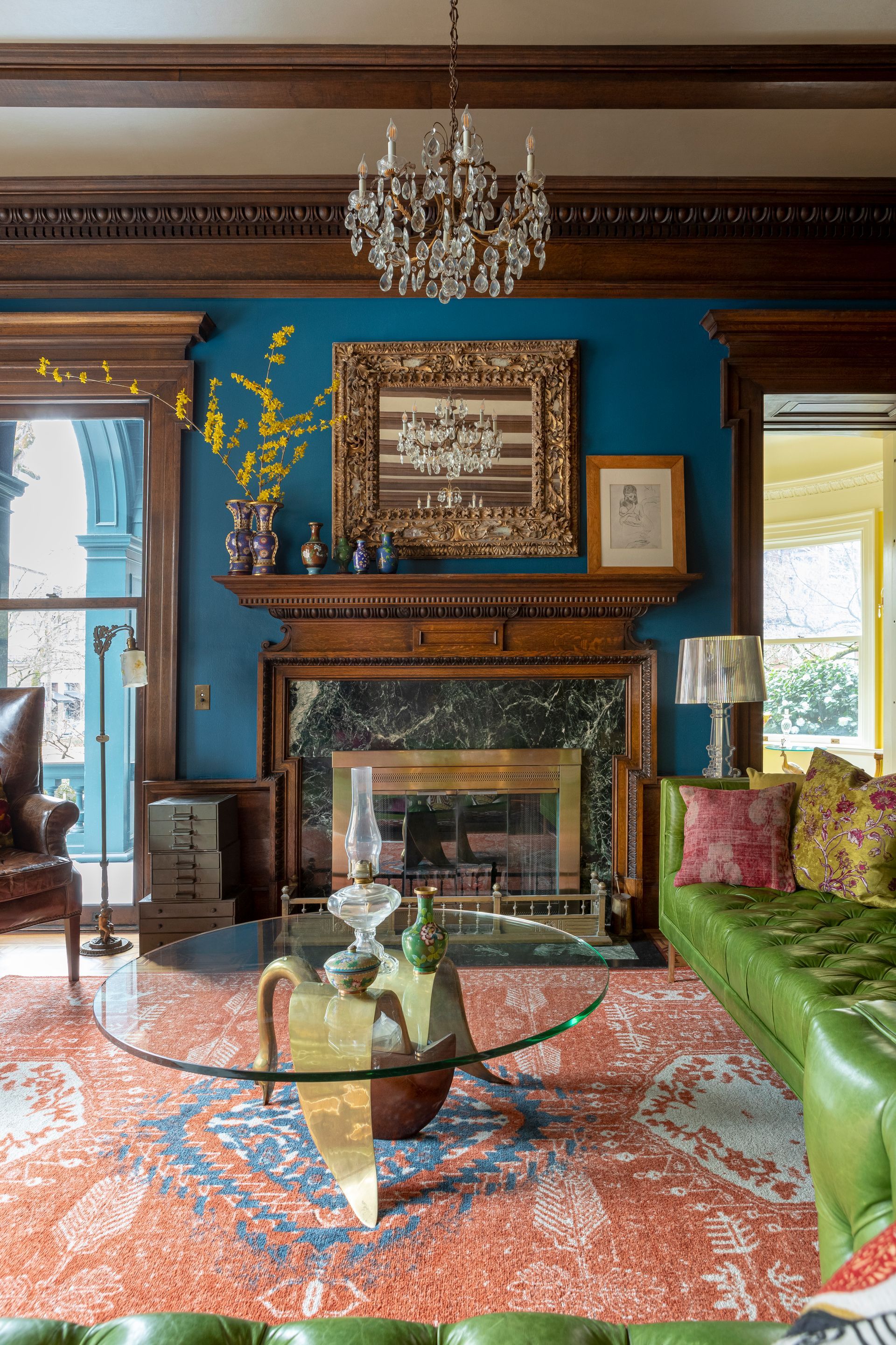 A living room featuring elaborate oak millwork and jewel tones with eclectic furnishings, focused around a large fireplace.