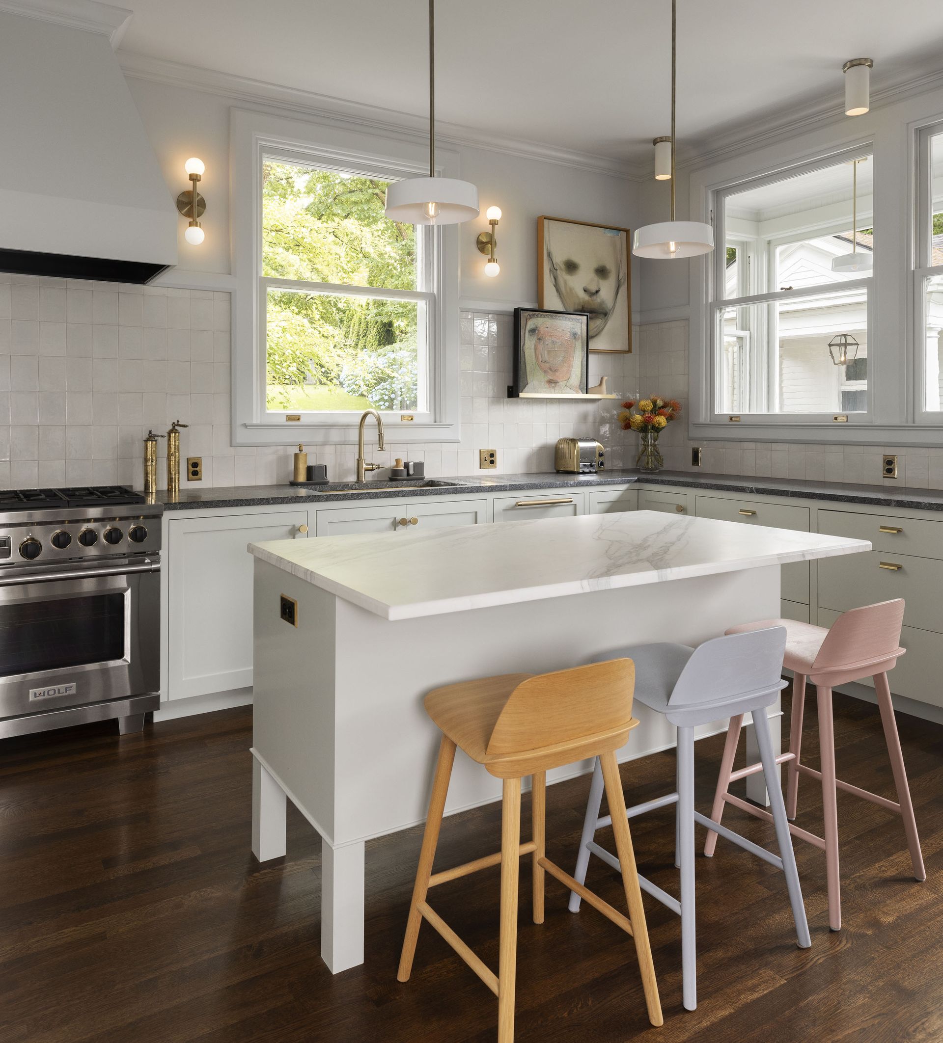 A remodeled colonial kitchen with custom cabinetry, Danish stools at the island, and contemporary art and fixtures.