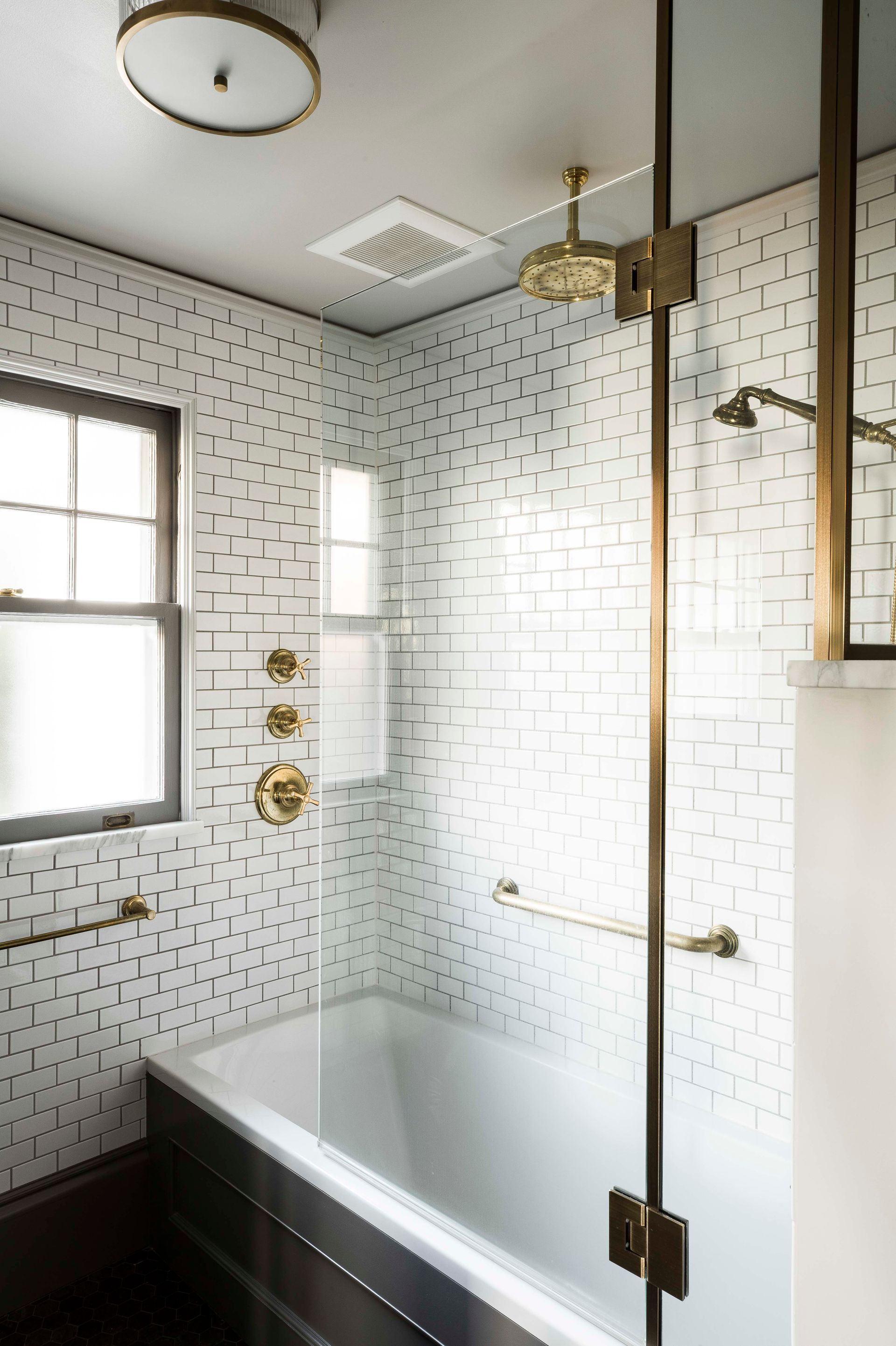 The main bathroom has gray stone hex floor tile, white glazed wall tile, unlacquered brass hardware and plumbing fixtures.